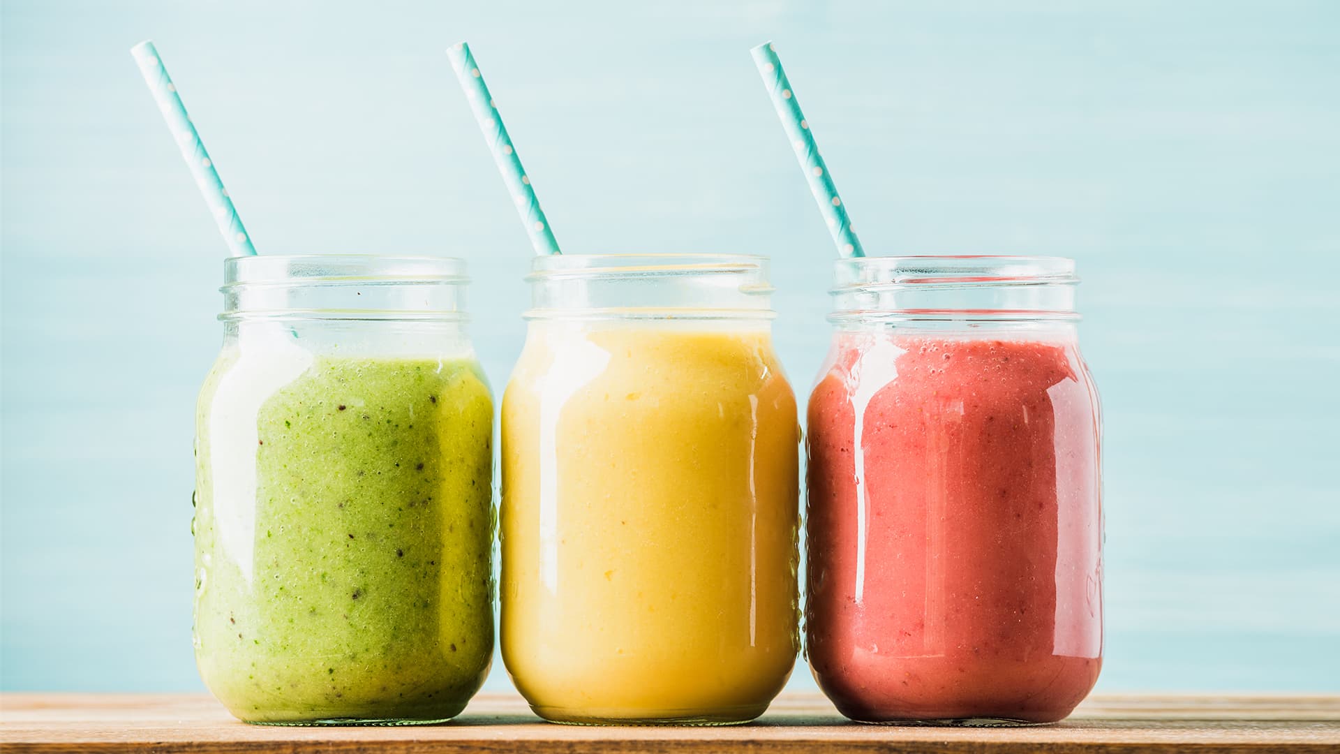 Green, hello and pink smoothies in jars with straws