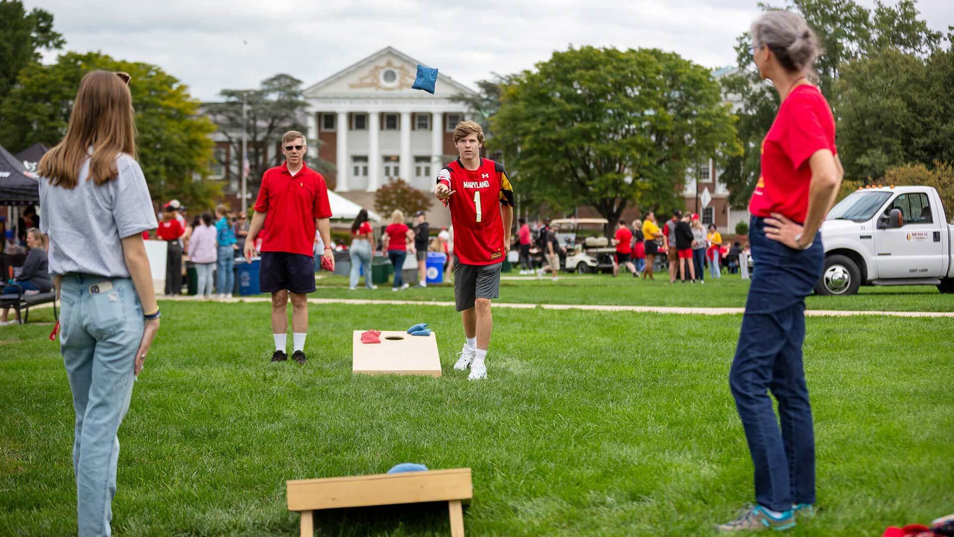 two men play conrhole against two women in front of the UMD main administration building