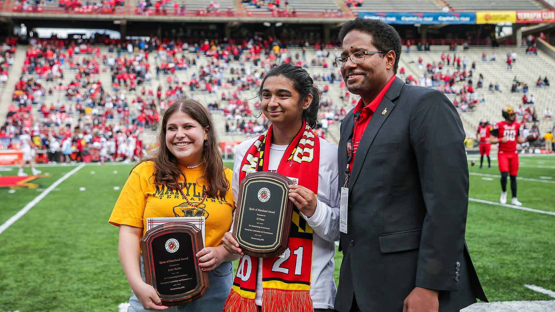 Spirit of Maryland Award winners Josie Shaffer, left and M. Pease are honored on Capital One Field with President Darryll J. Pines.