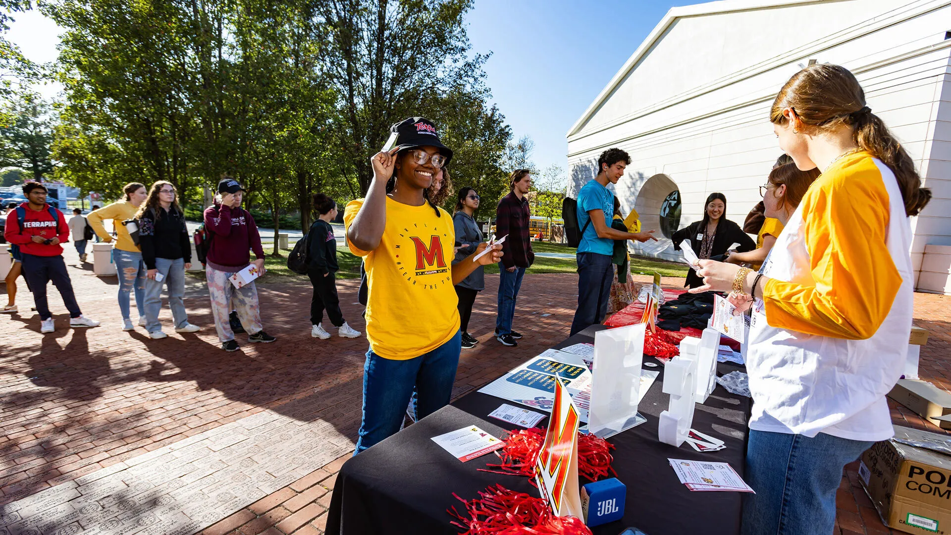a person stands at a table set up outdoors and receives a commorative hat