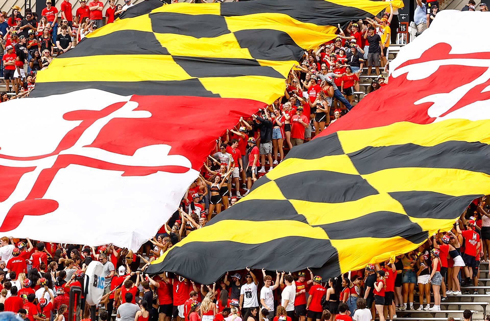 hundreds of students in a stadium hold up a giant bipartite Maryland flag