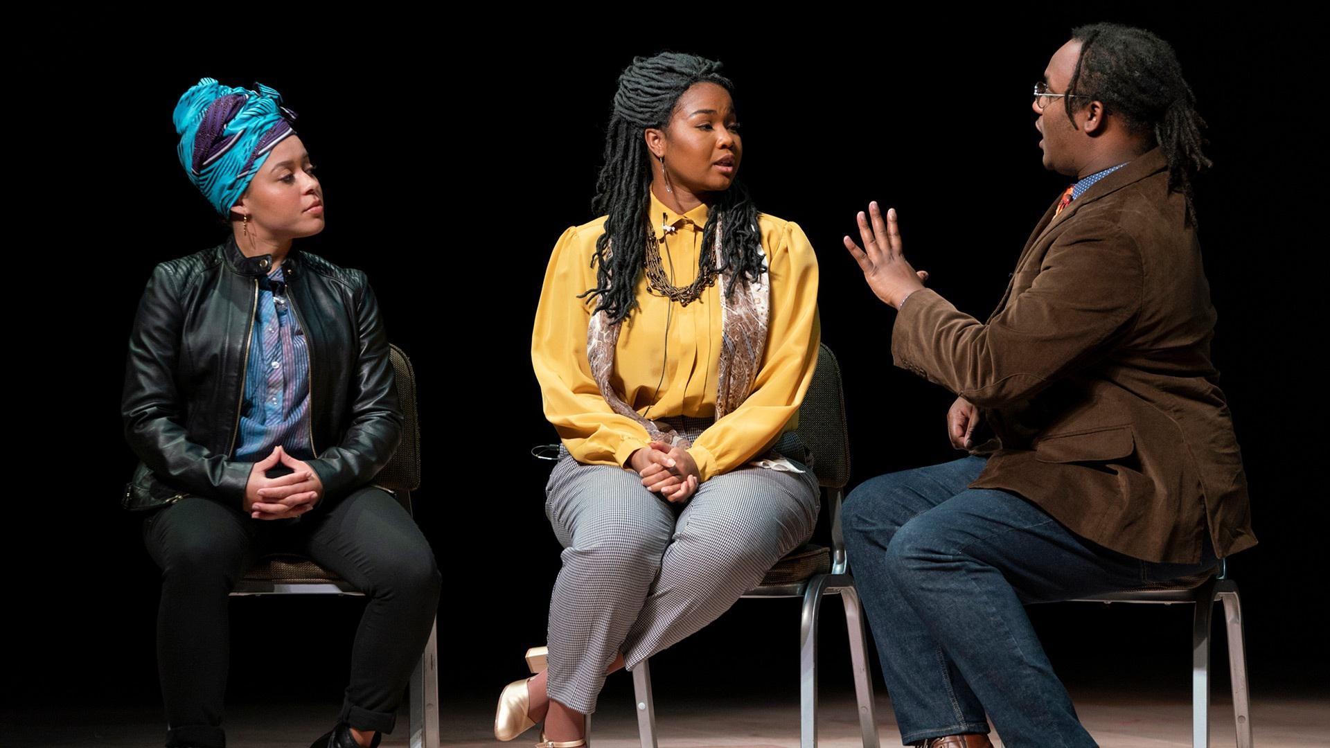 Three Black people talk while sitting on stools