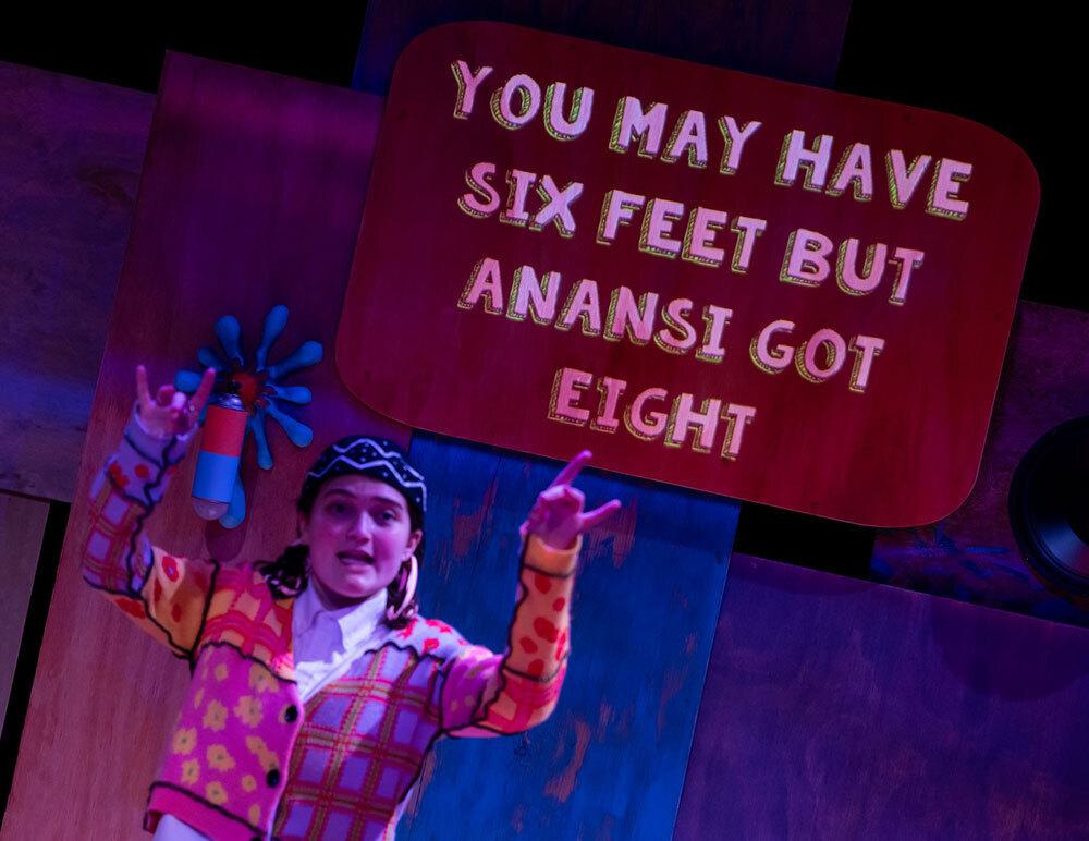 an actor gestures on a stage while a caption is projected above her head