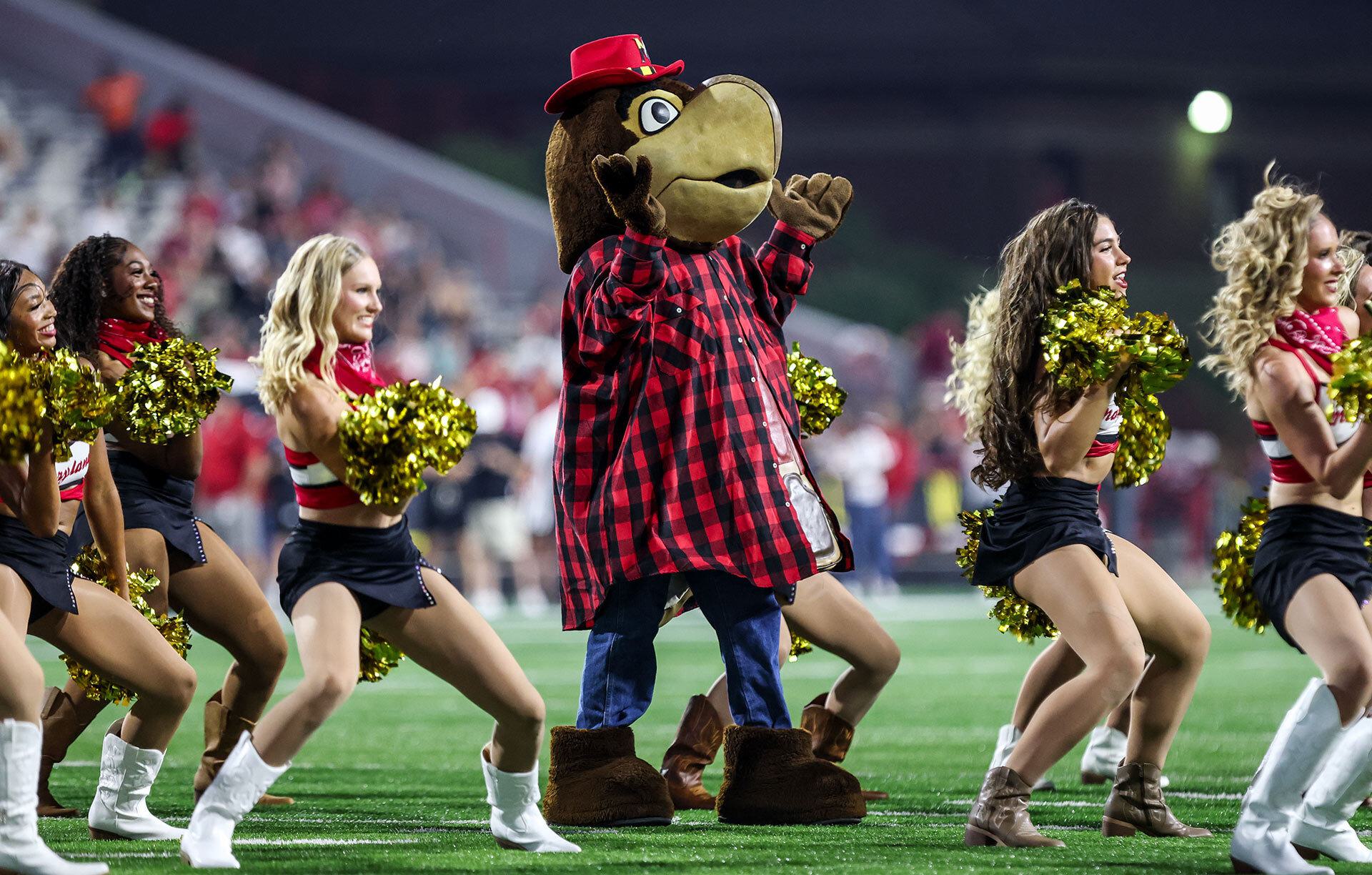 Testudo dances with dance team while wearing red flannel shirt and hat