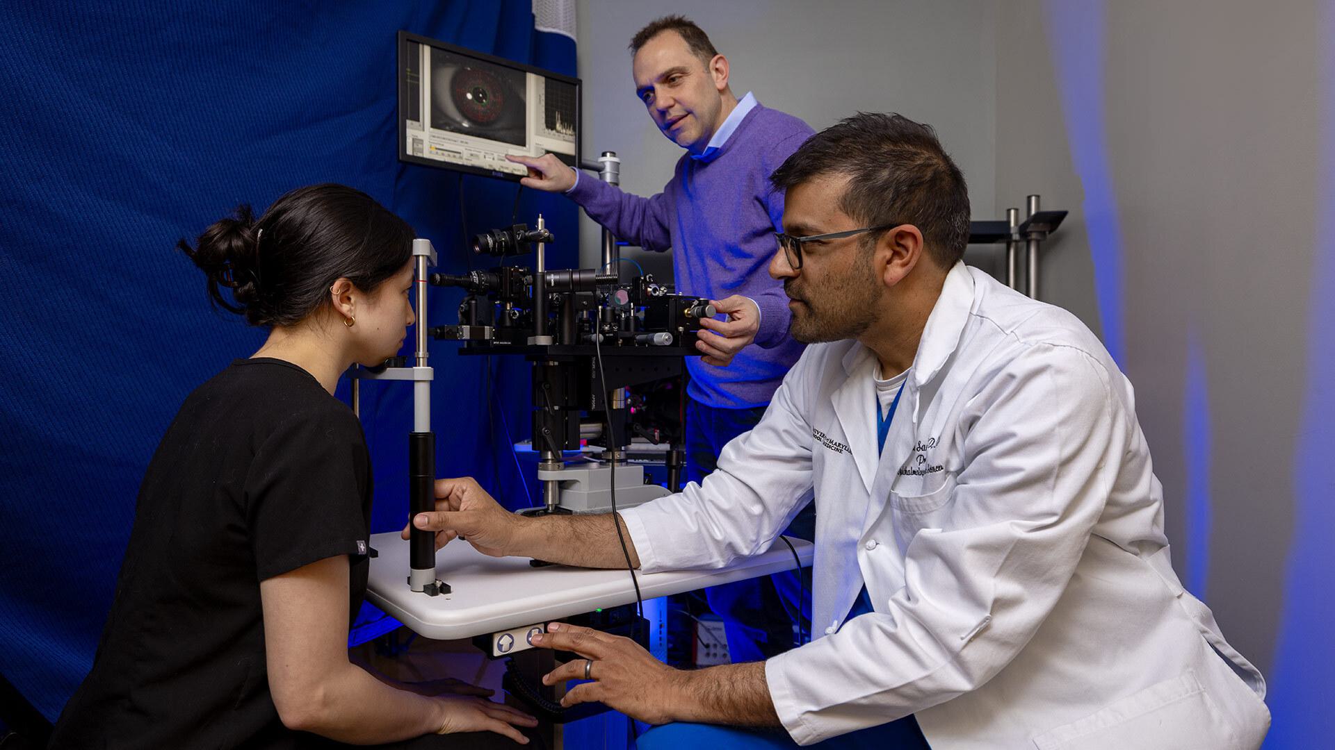Dr. Osamah J. Saeedi wears a white coat and works with a patient on an eye-screening machine