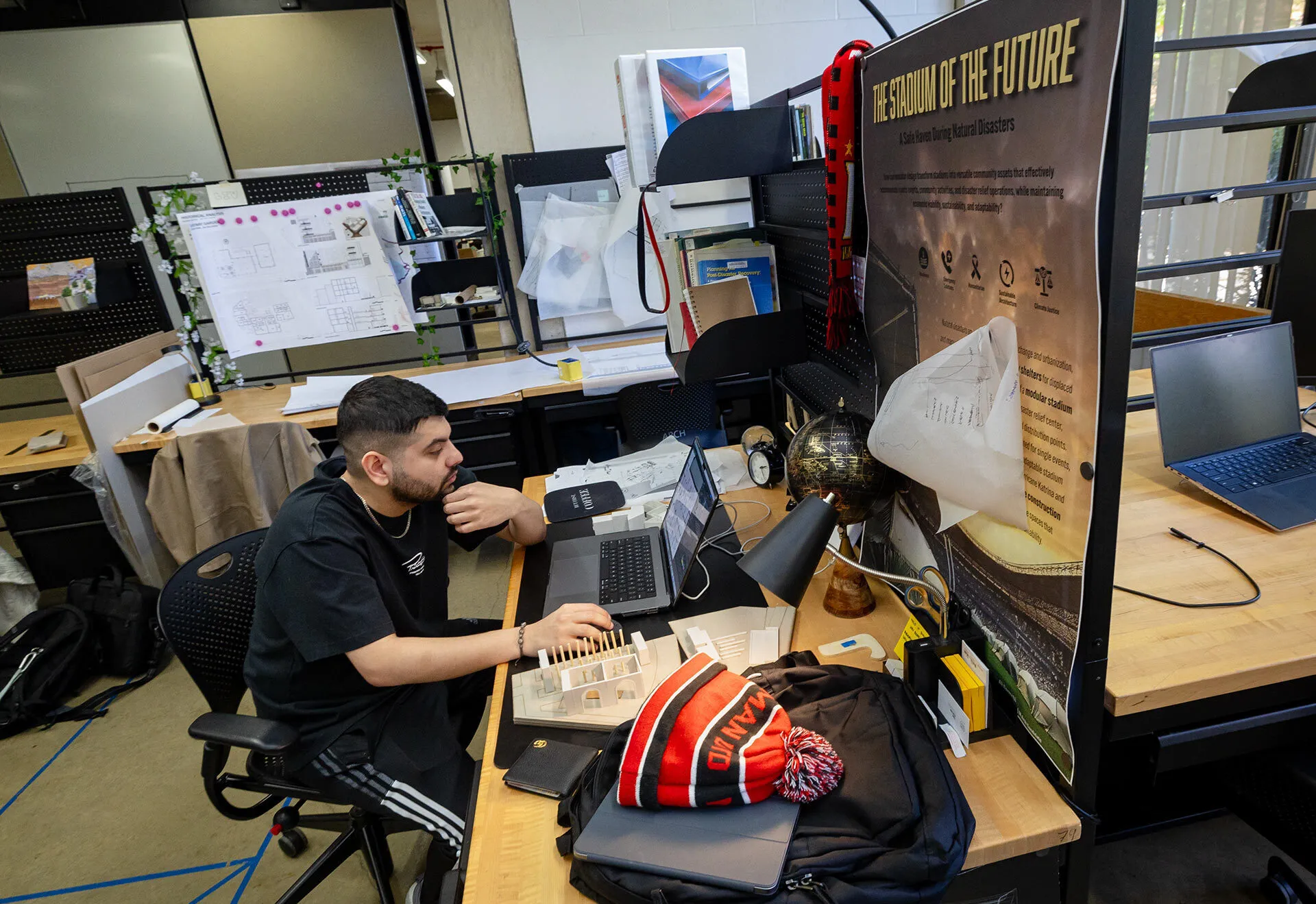 student works on his laptop on a desk with a Manchester United beanie and model construction projects