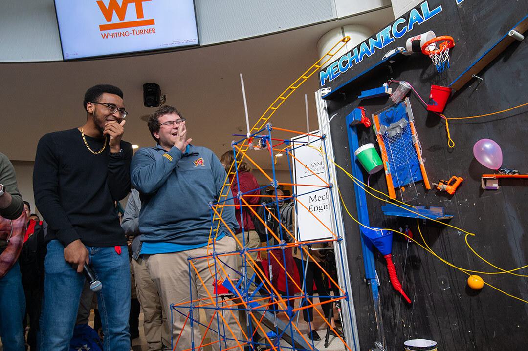 two students laugh looking at their rube goldberg machine