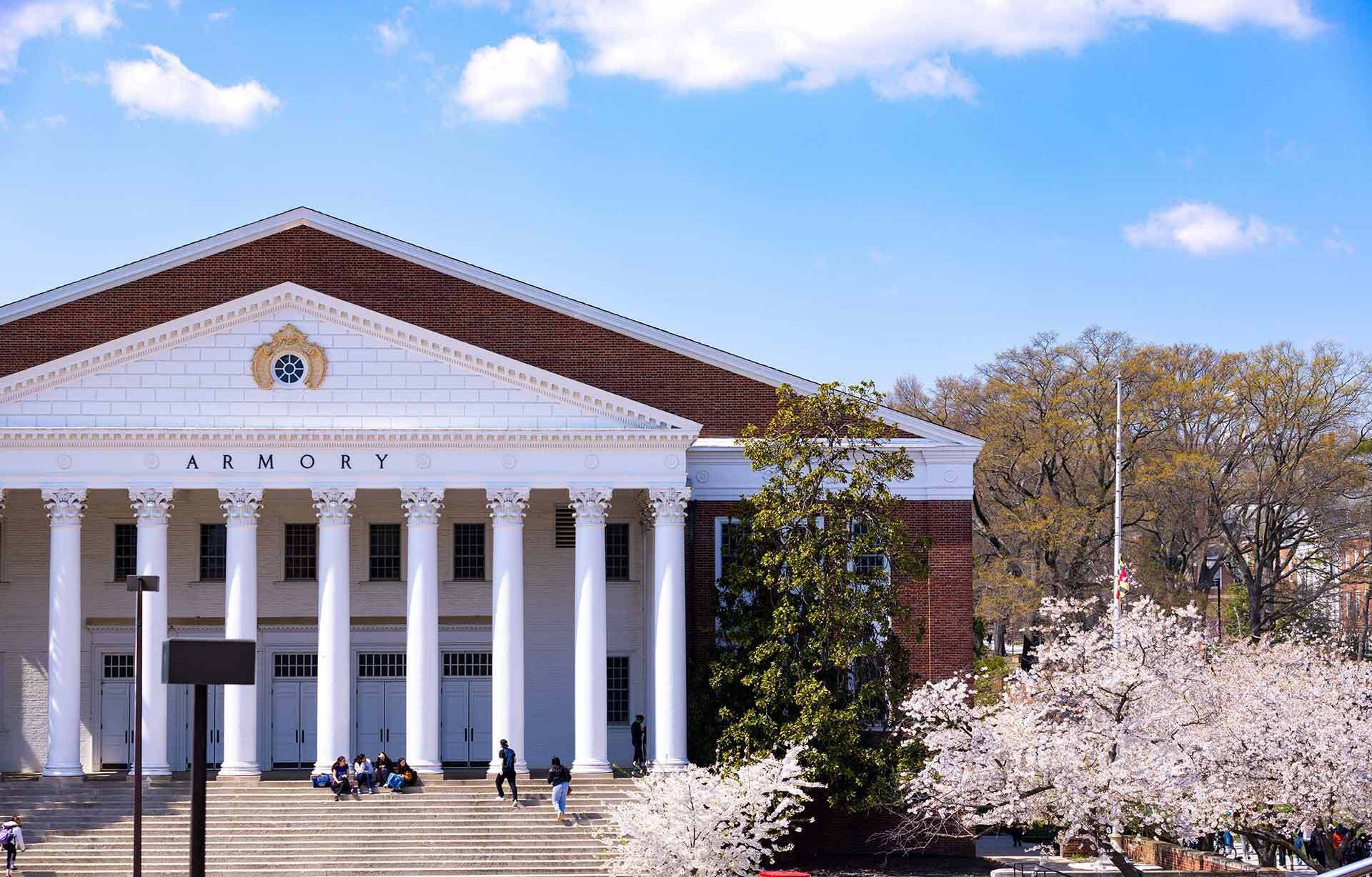 UMD Armory building with students on the steps and cherry blossoms to the side