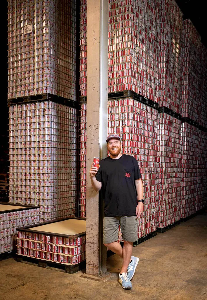 Man stands near large stack of empty beer cans