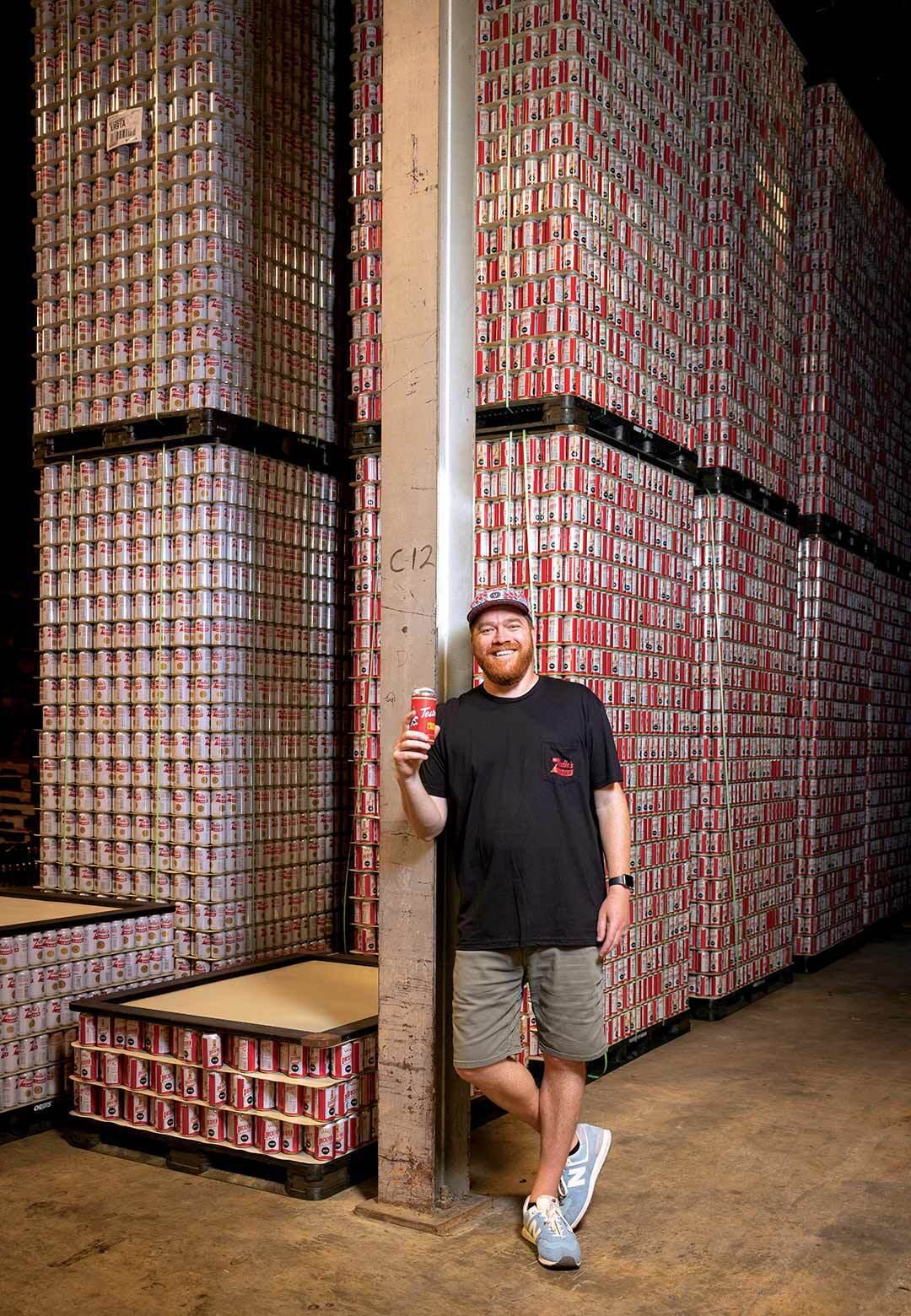 Man stands near large stack of empty beer cans