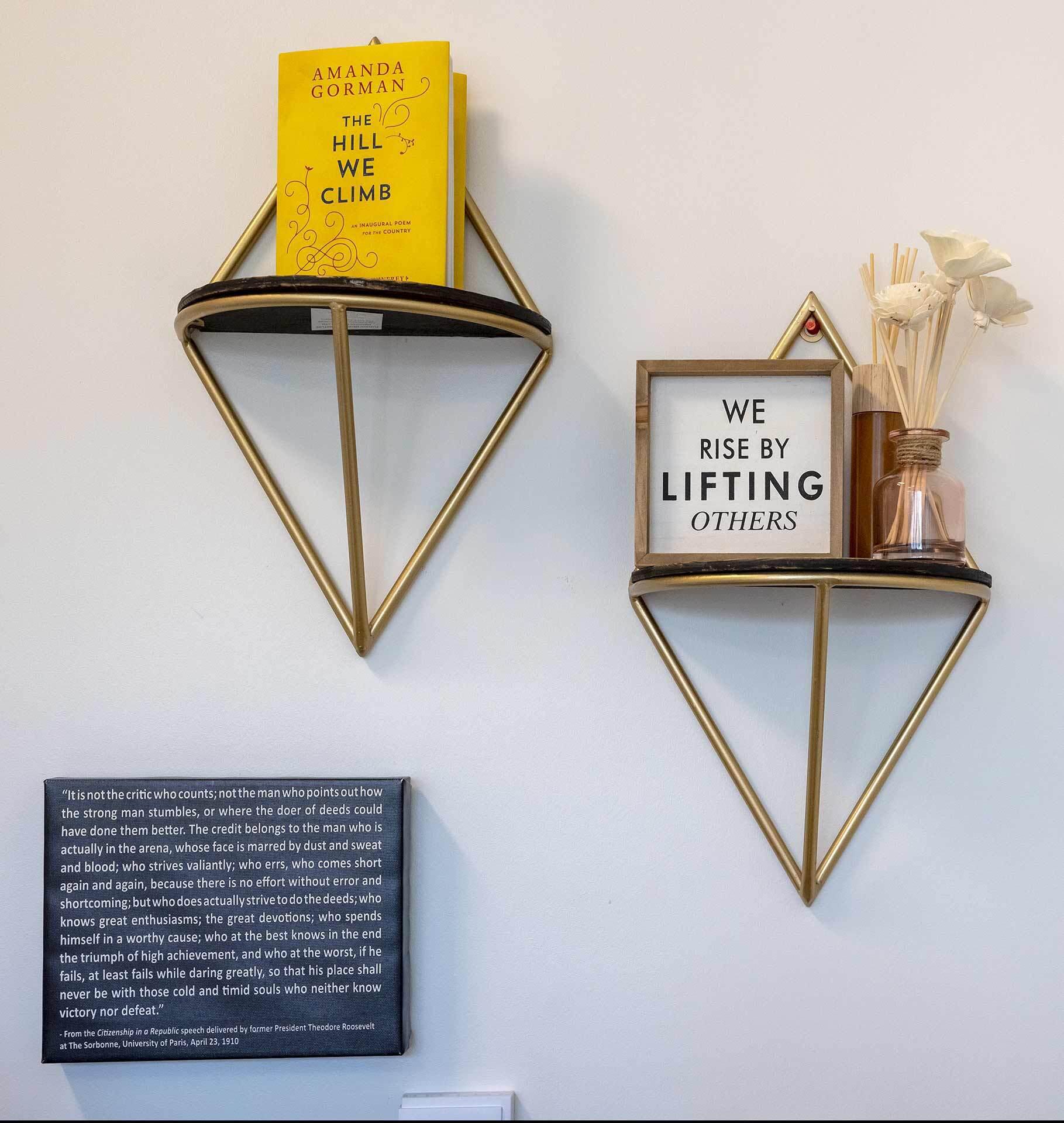 Amanda Gorman's book "The Hill We Climb," a plaque that says "We rise by lifting others" and white words on a black background from Theodore Roosevelt's "Man in the Arena" speech