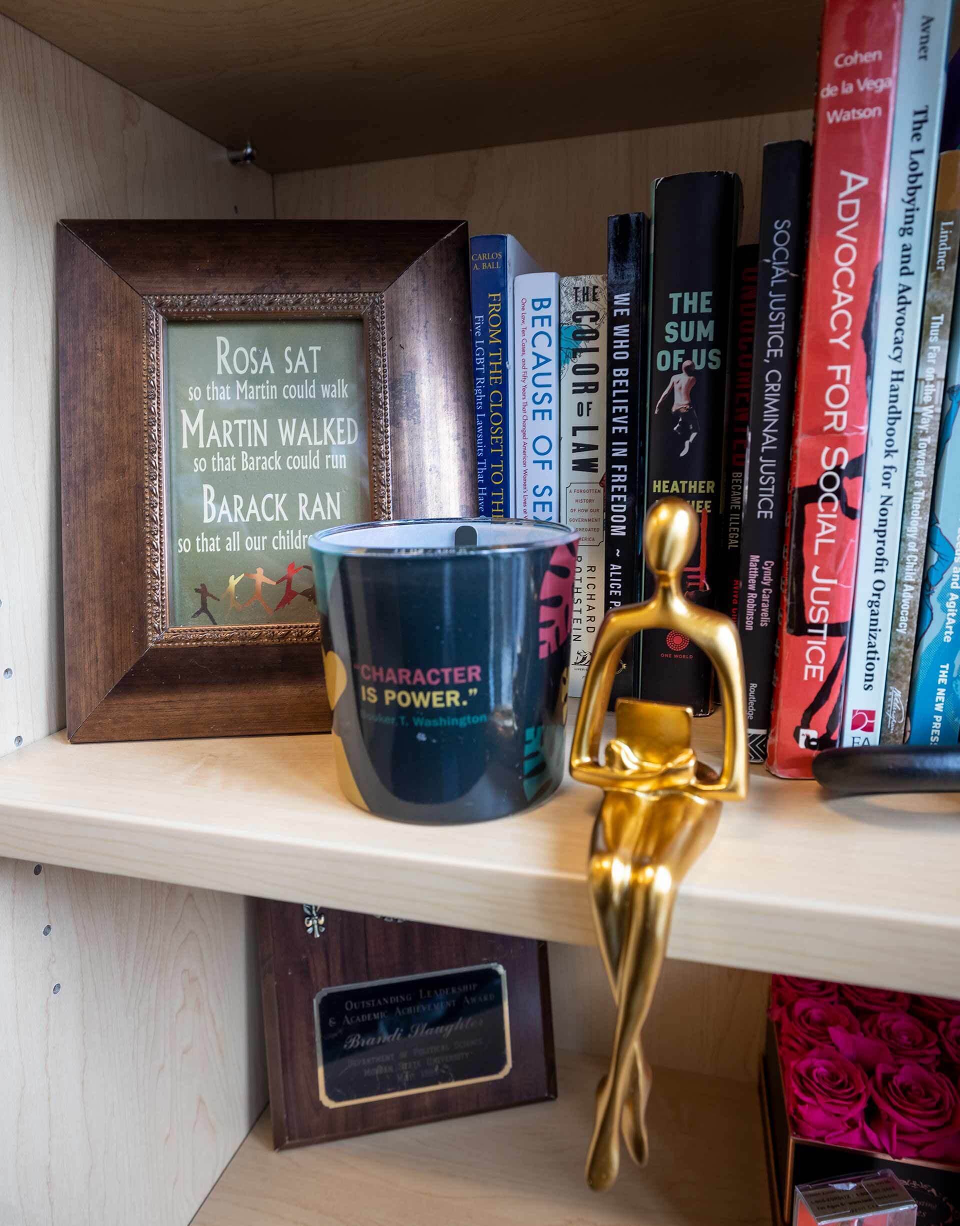 a framed postcard, a mug and a golden statue sit on a white bookshelf