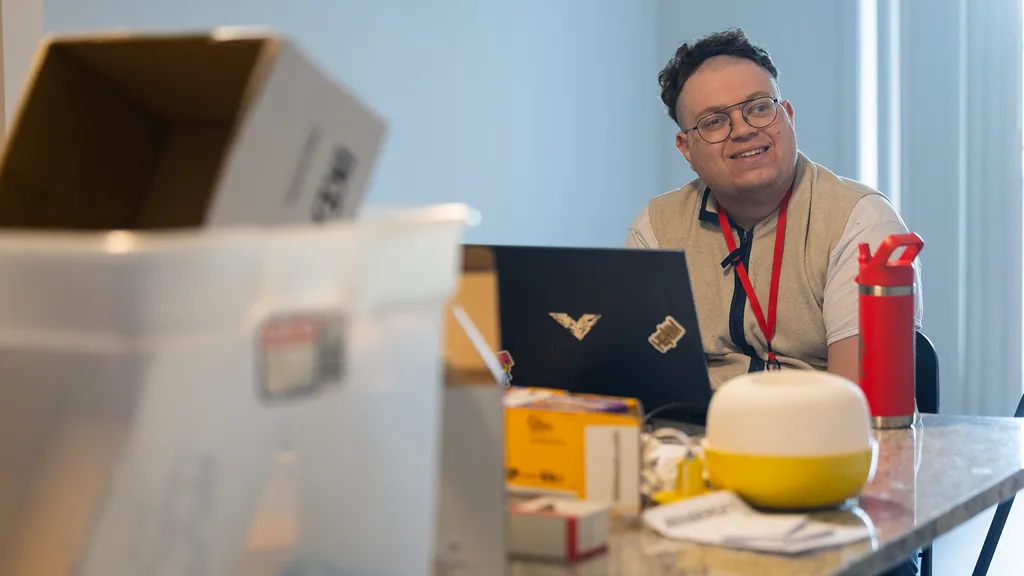 man smiles in kitchen of new apartment as he works on laptop