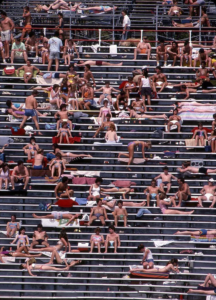 students sunbathe in swimsuits in football stadium stands
