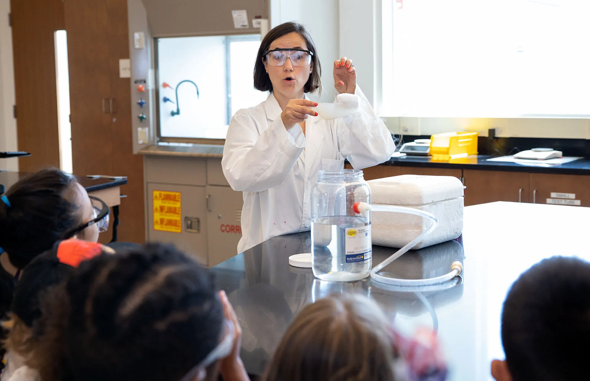 lecturer wearing white lab coat and goggles demonstrates for class