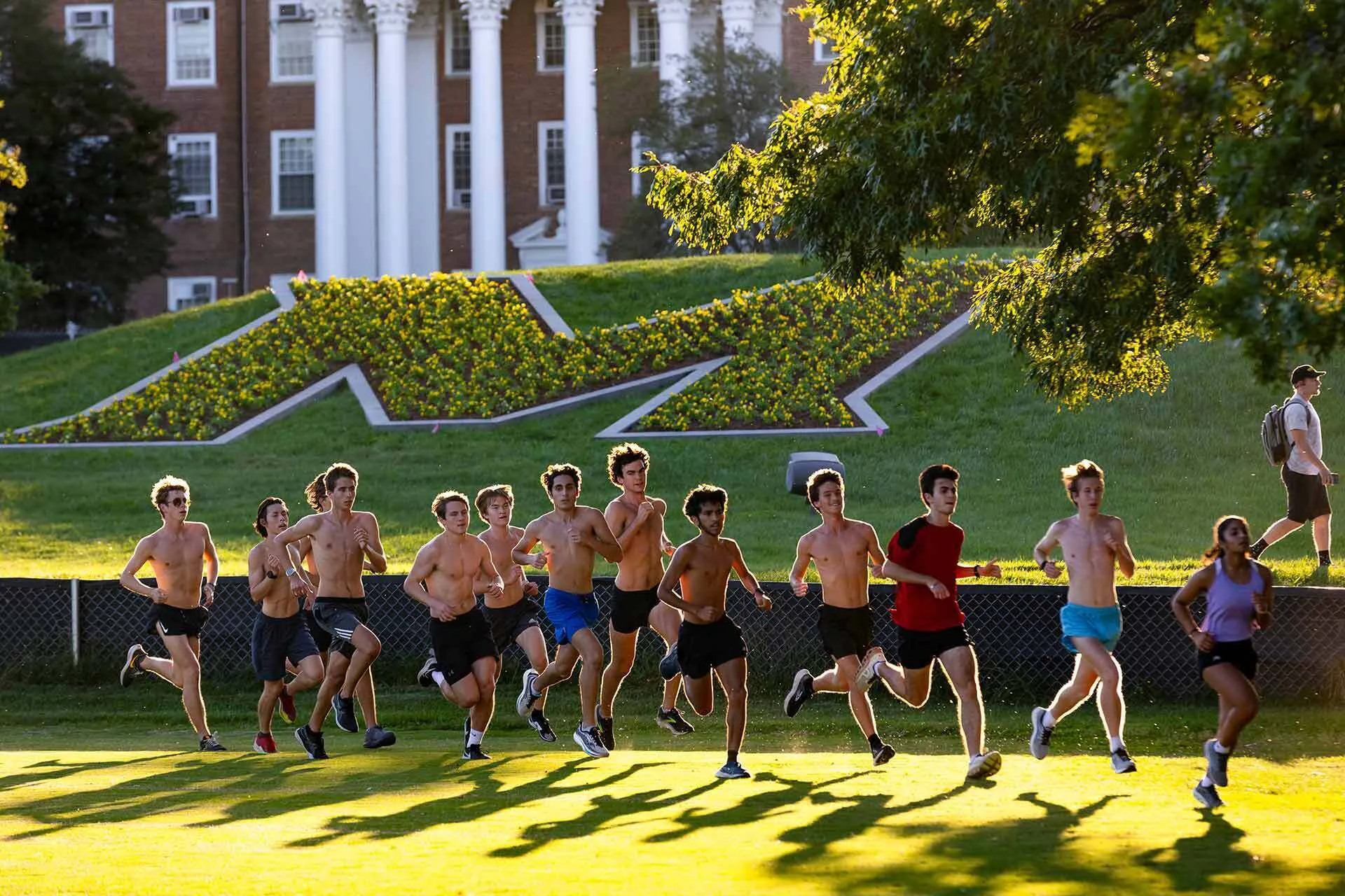 Male shirtless students run past the M planted with flowers