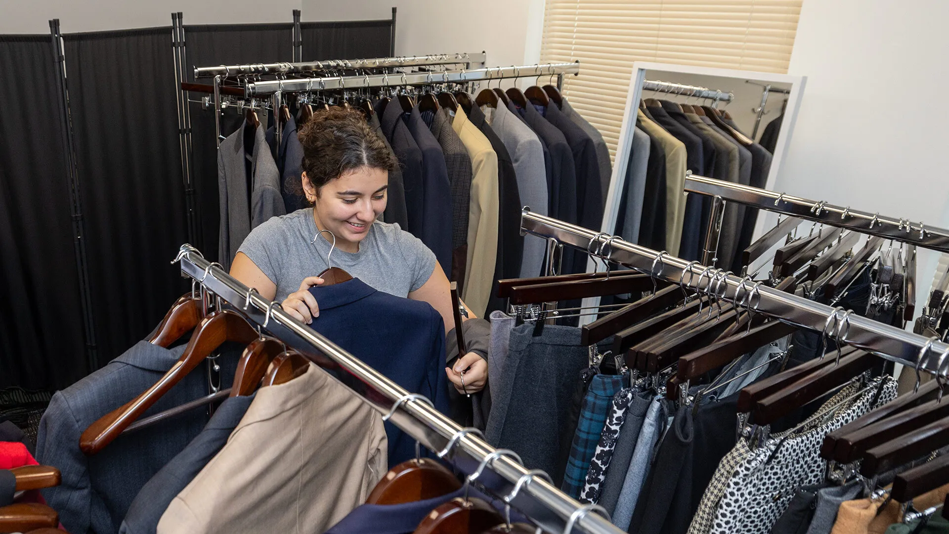 A female student in a gray shirt browses racks of clothing.
