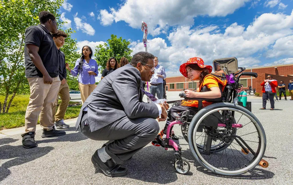 Darryll Pines speaks to Stella Stakolosa as she wears a red Terps hat and sits in her wheelchair