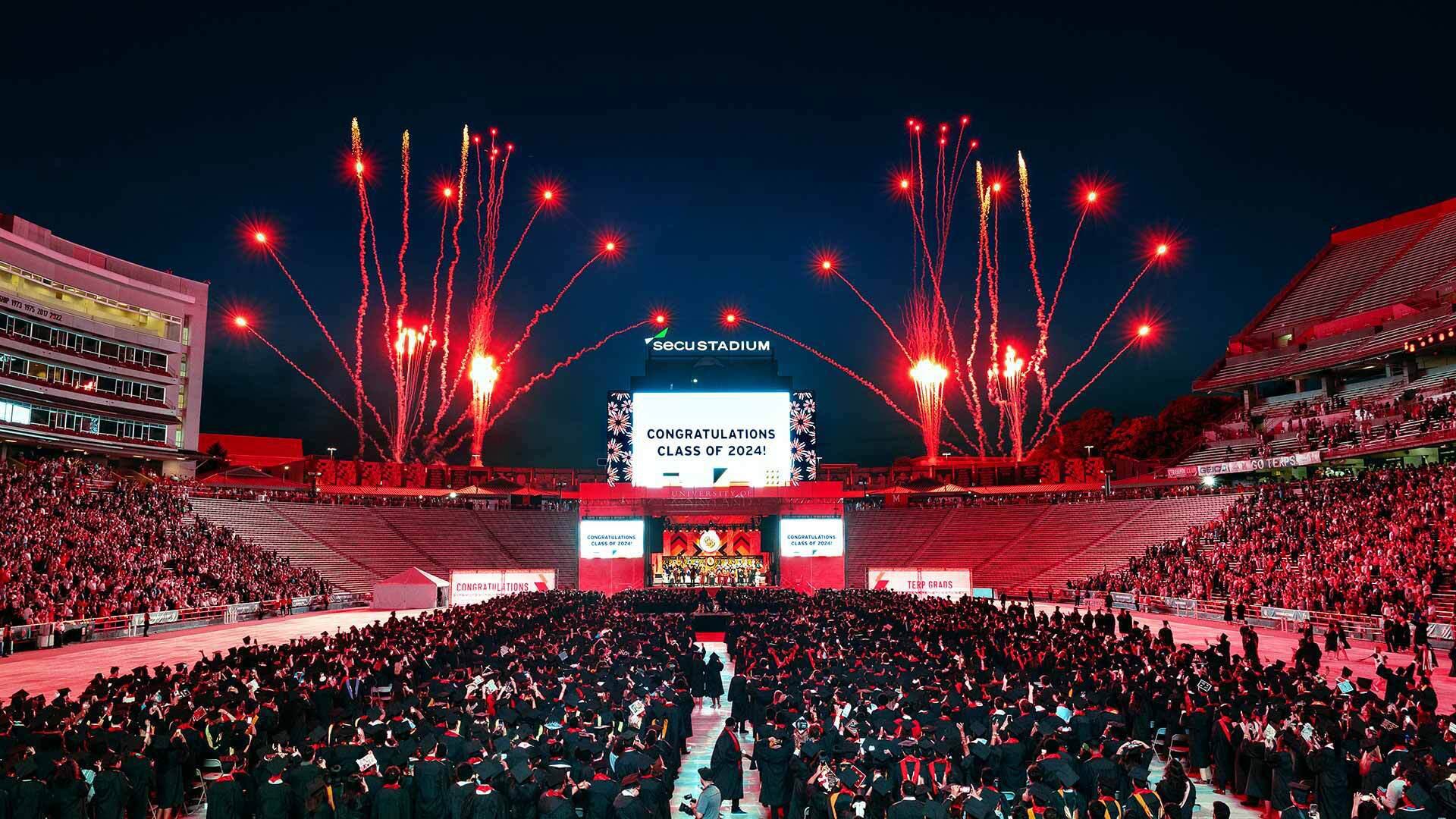 graduates watch red fireworks over SECU stadium
