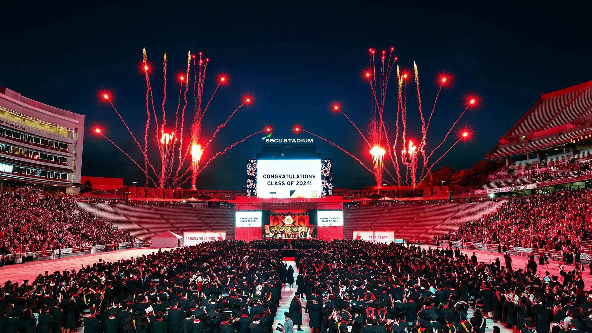 graduates watch red fireworks over SECU stadium