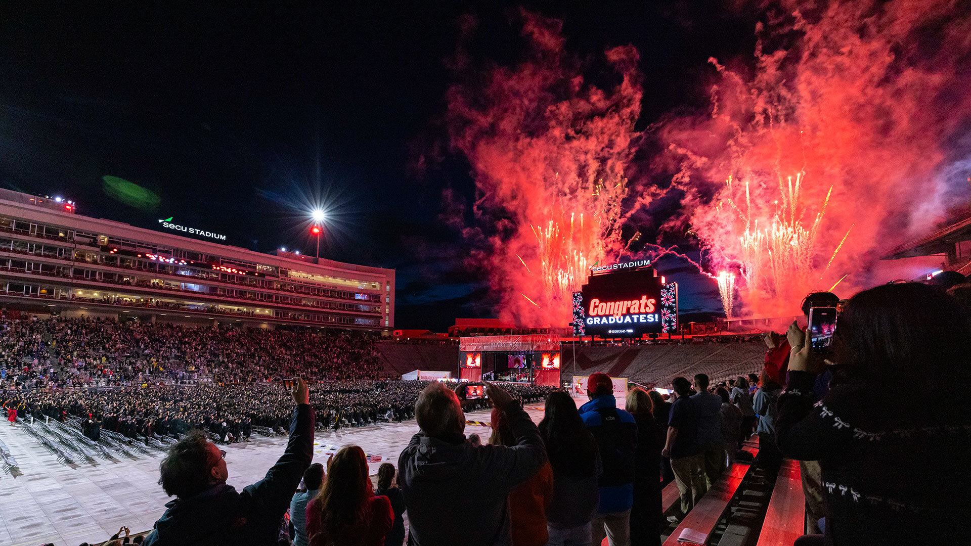 red fireworks with "Congrats graduates" flashing on scoreboard at SECU Stadium