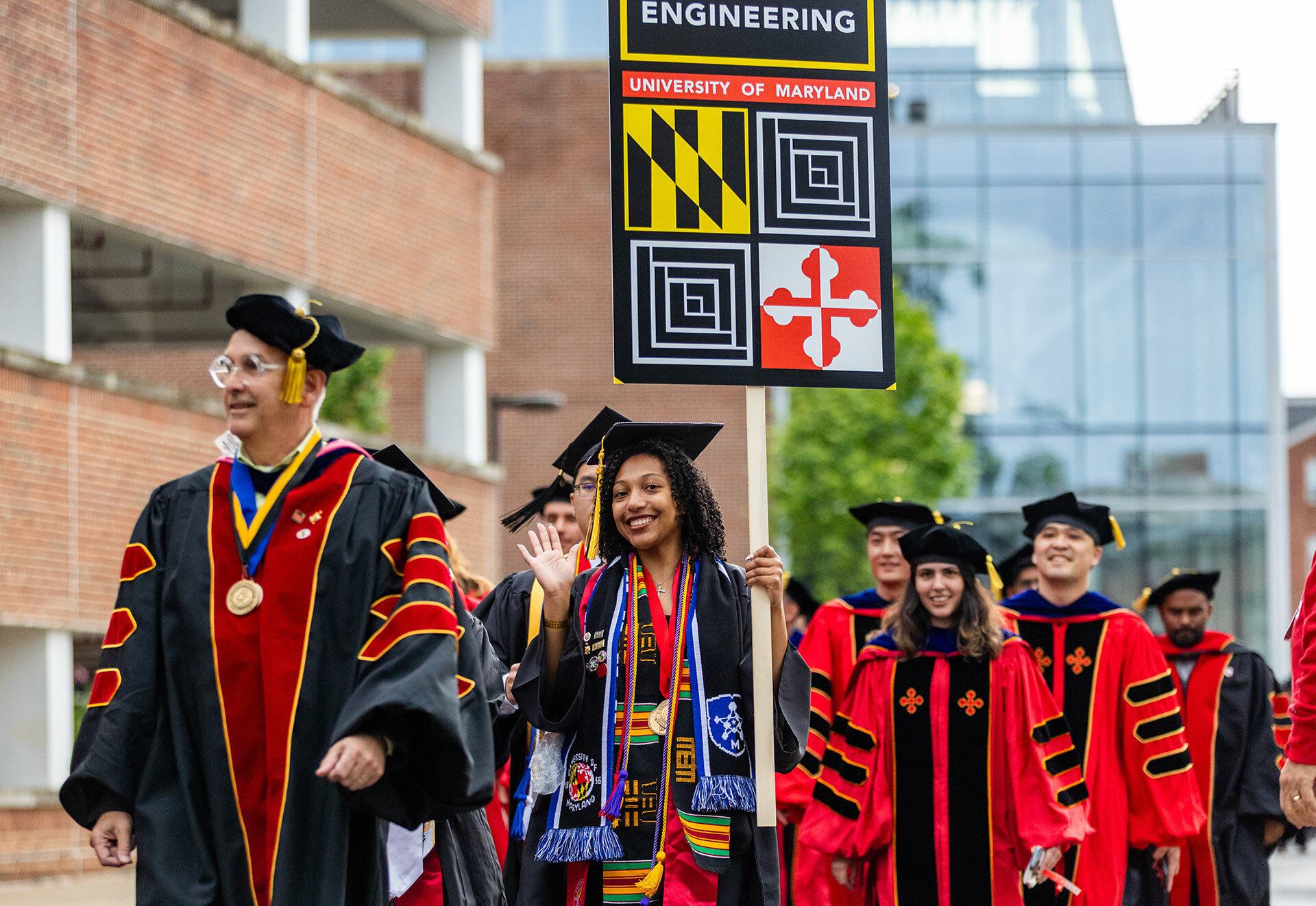 student carries engineering gonfalon as she leads fellow grads