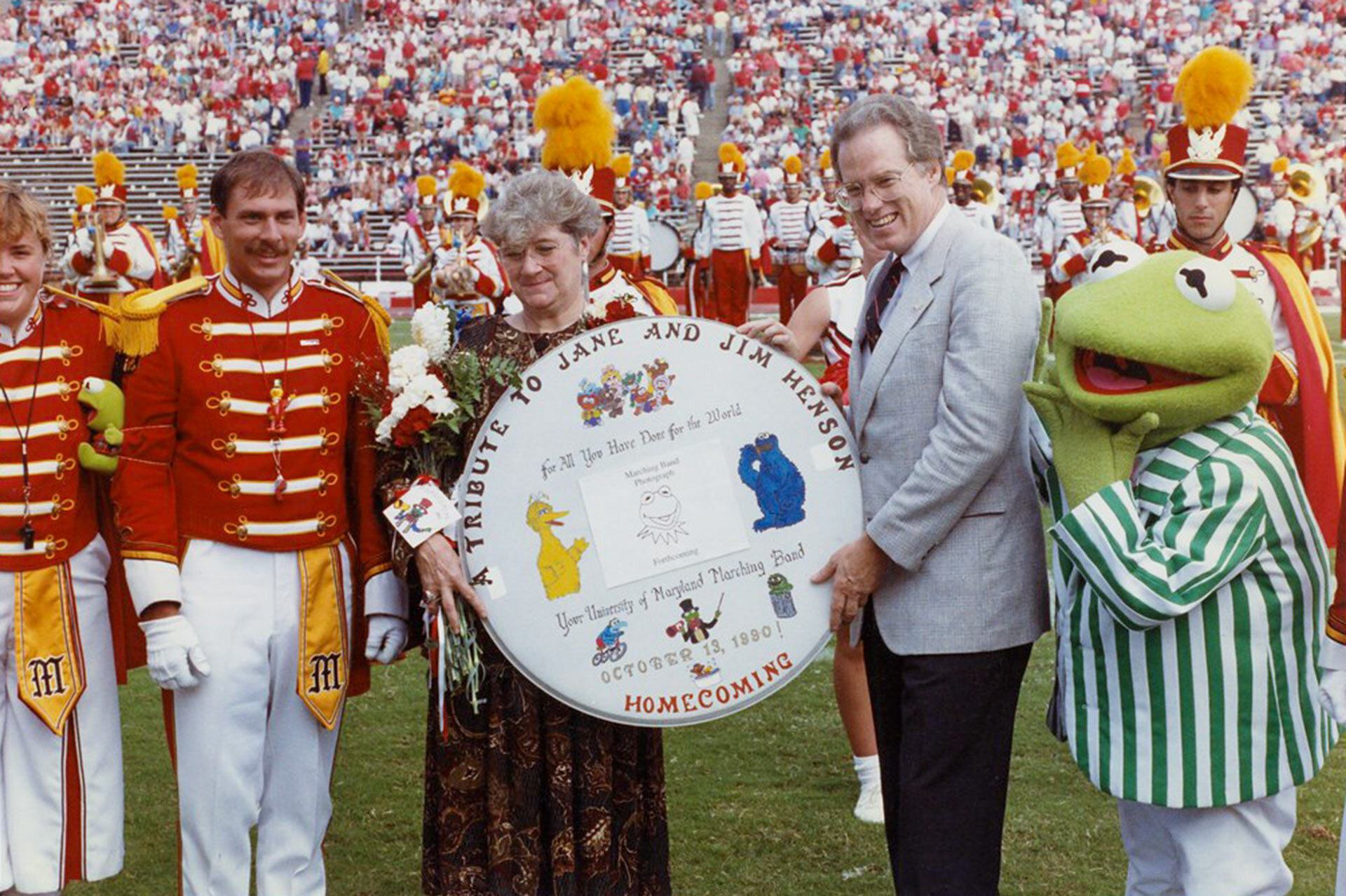 Jane Henson and Brit Kirwan hold a tribute to Jim Henson with marching band members and a life-size Kermit the Frog looking on