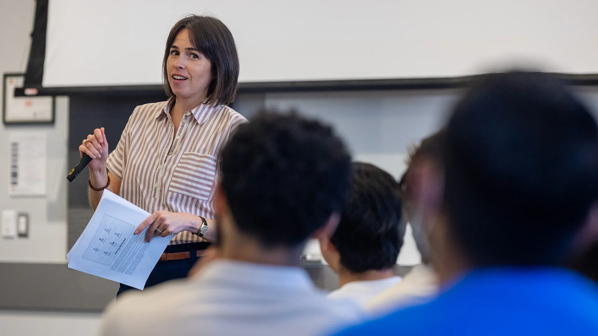 Sara Herald in a striped brown and white button-down lectures in class