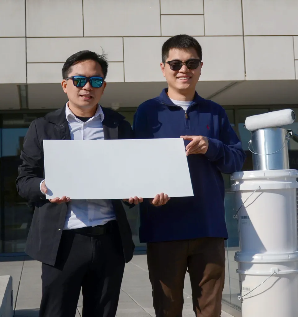 two men hold a white rectangular piece of metal in front of a white building