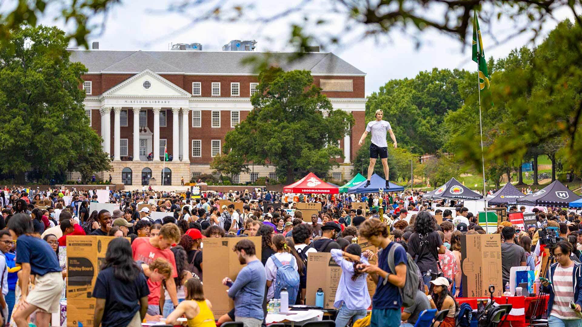 one student soars above crowd of students and tents on McKeldin Mall