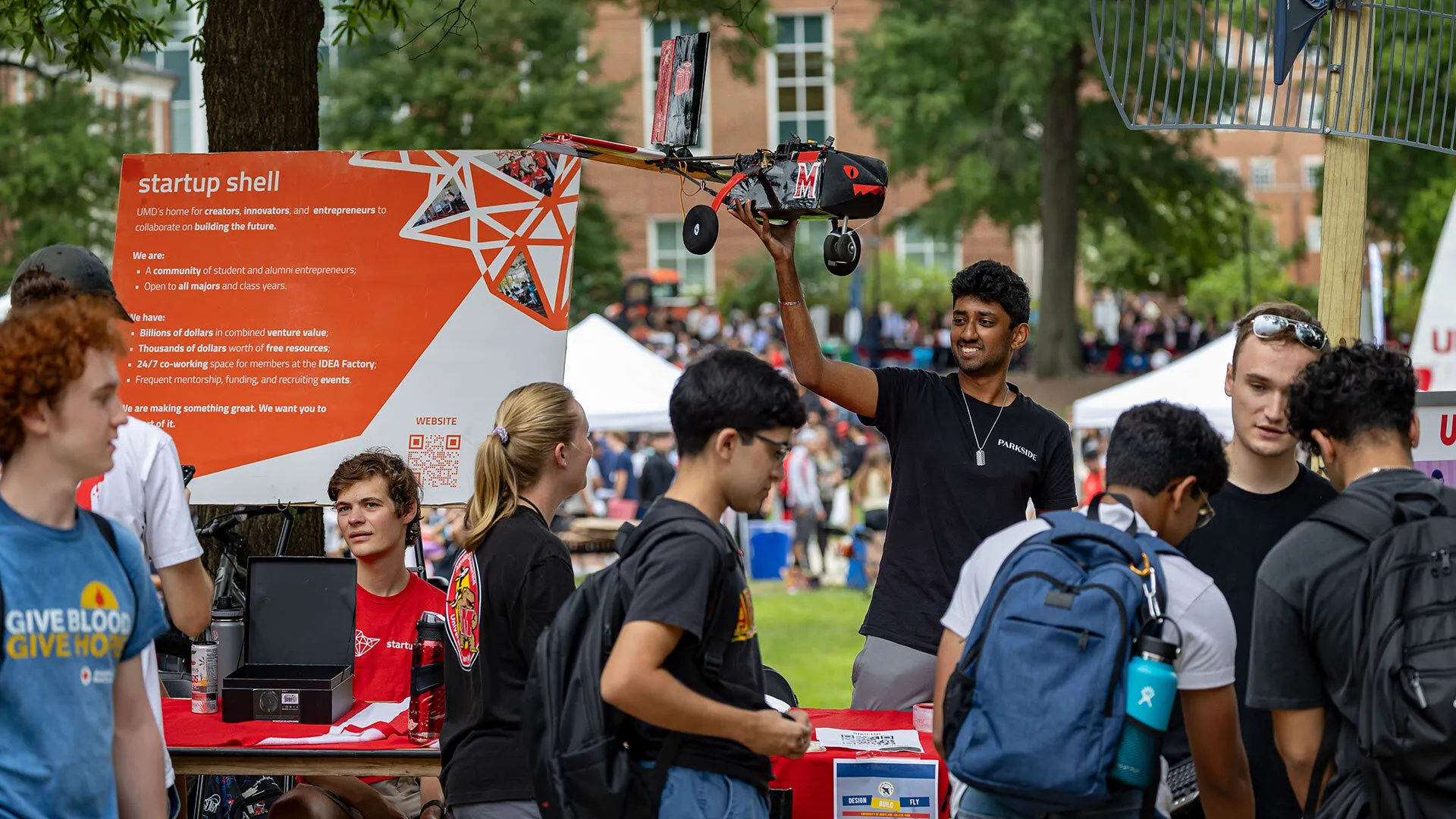 student holds up small plane as other students mingle at First Look Fair