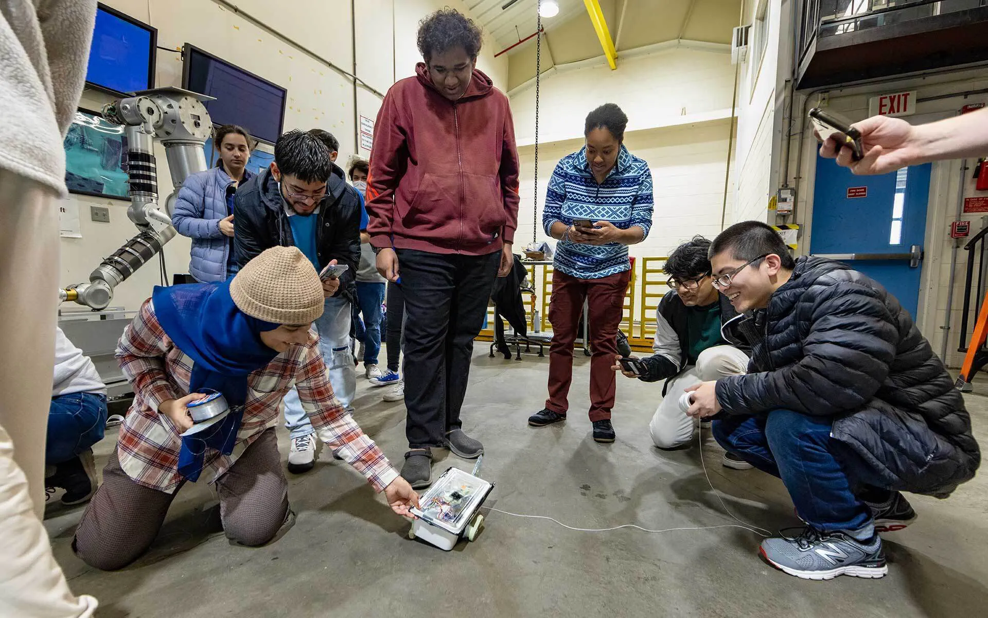 Students gather around a small robot on the floor