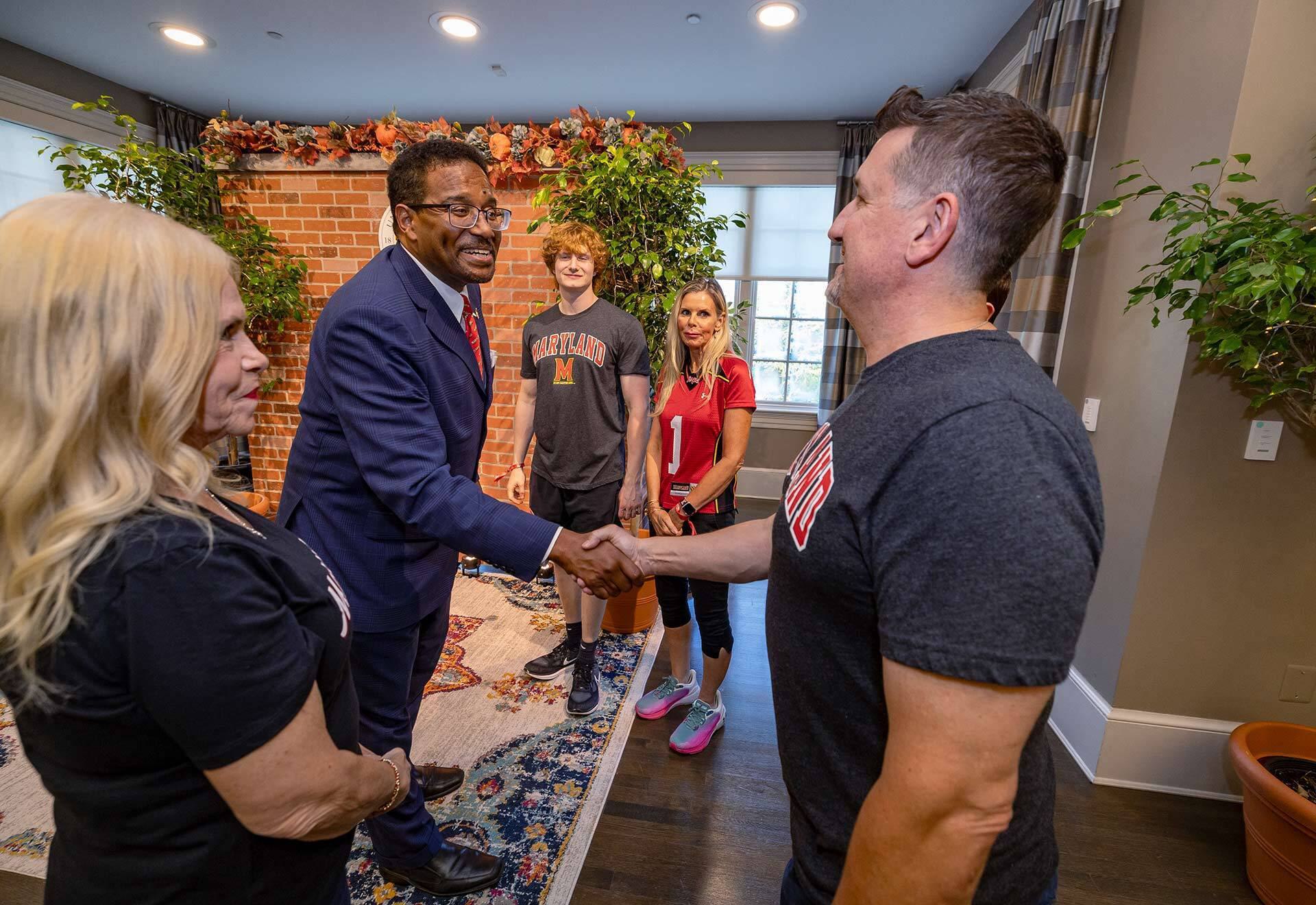 two men shake hands and two women and a young man observe