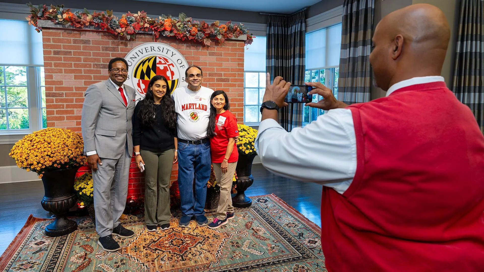 A university president and three members of a family including a student pose in a room, everyone smiling