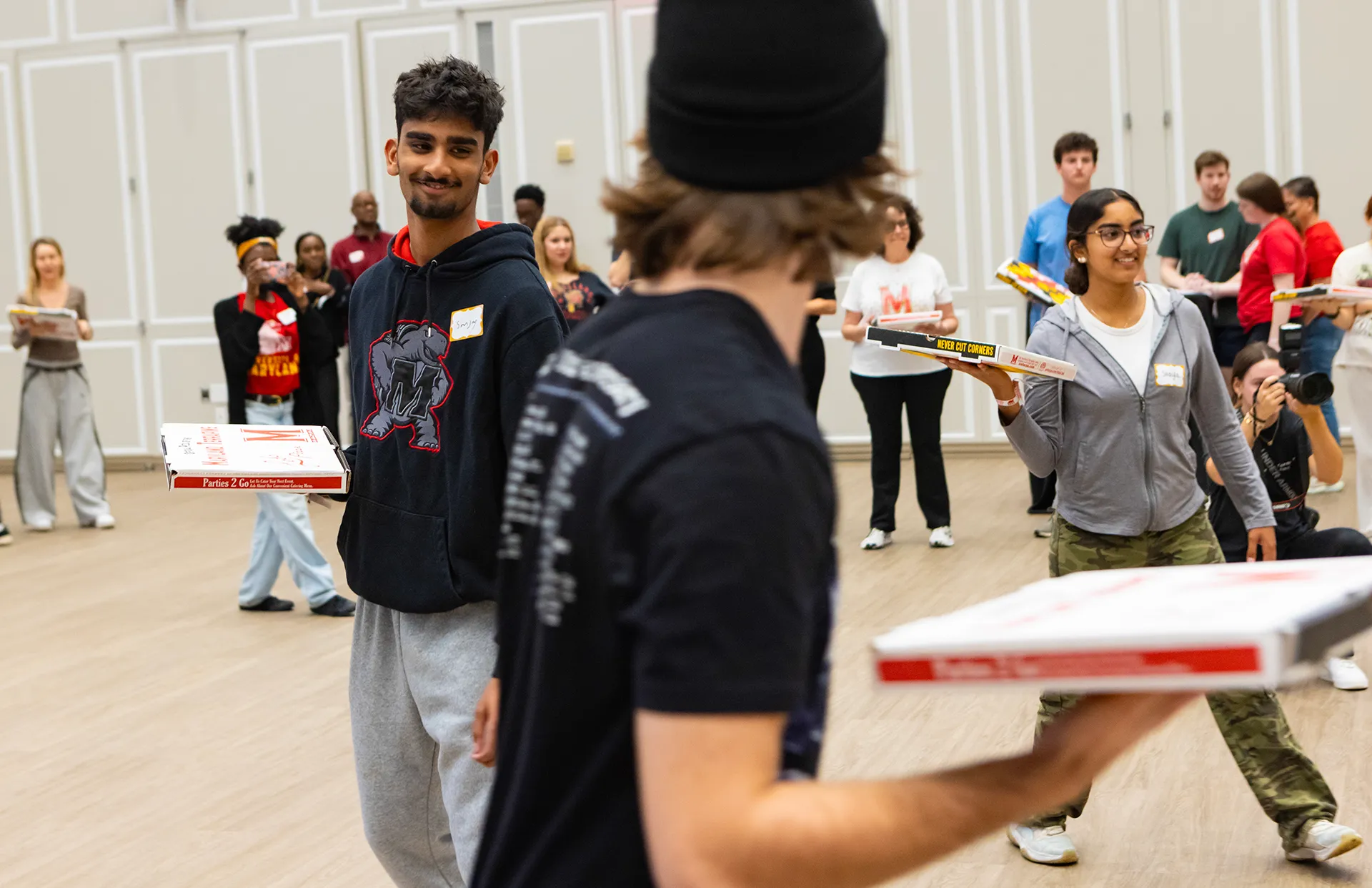 Two people play a game holding boxes of Ledo pizza in a large room