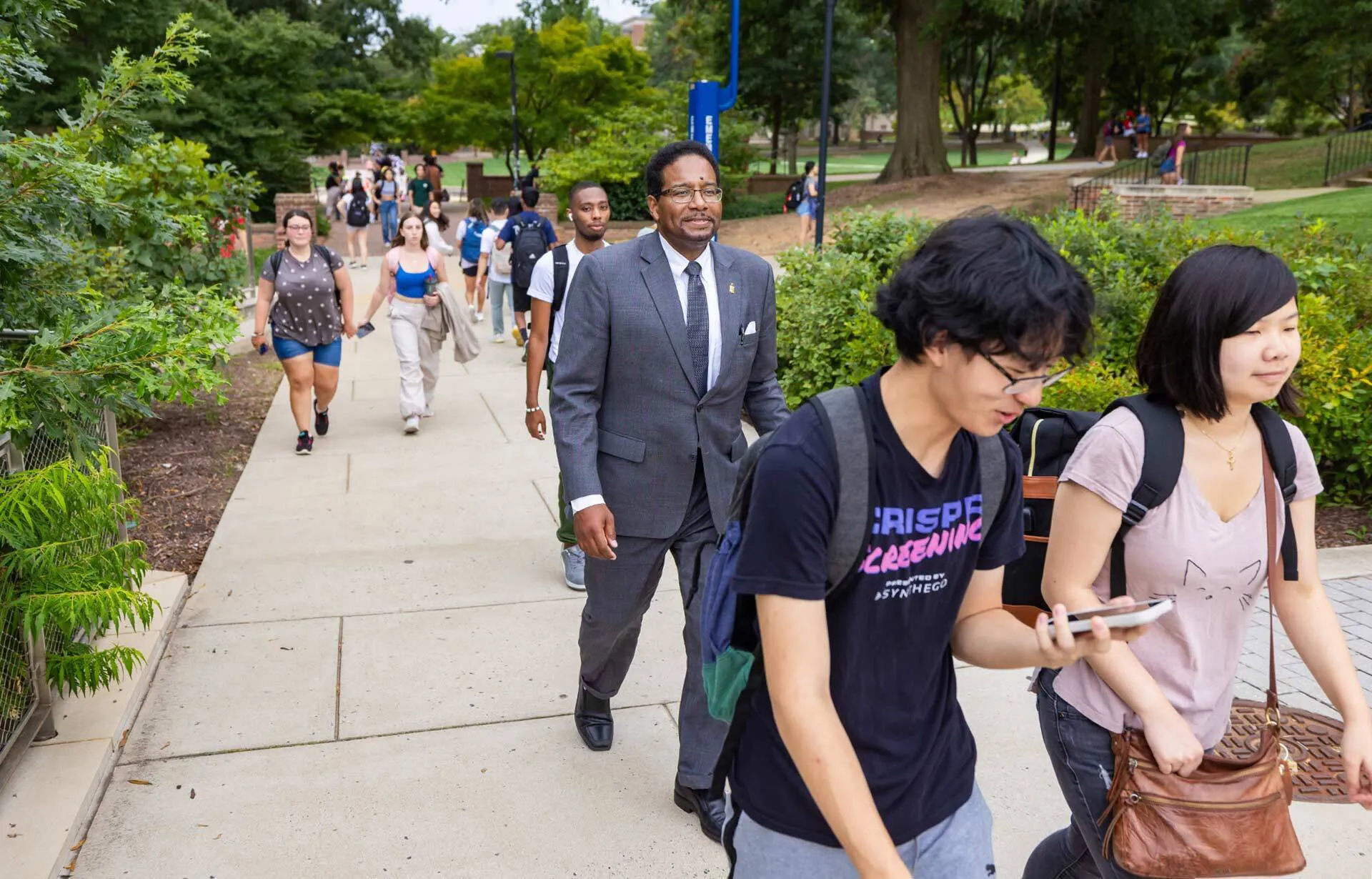 Darryll Pines in a suit walks with students on a sidewalk