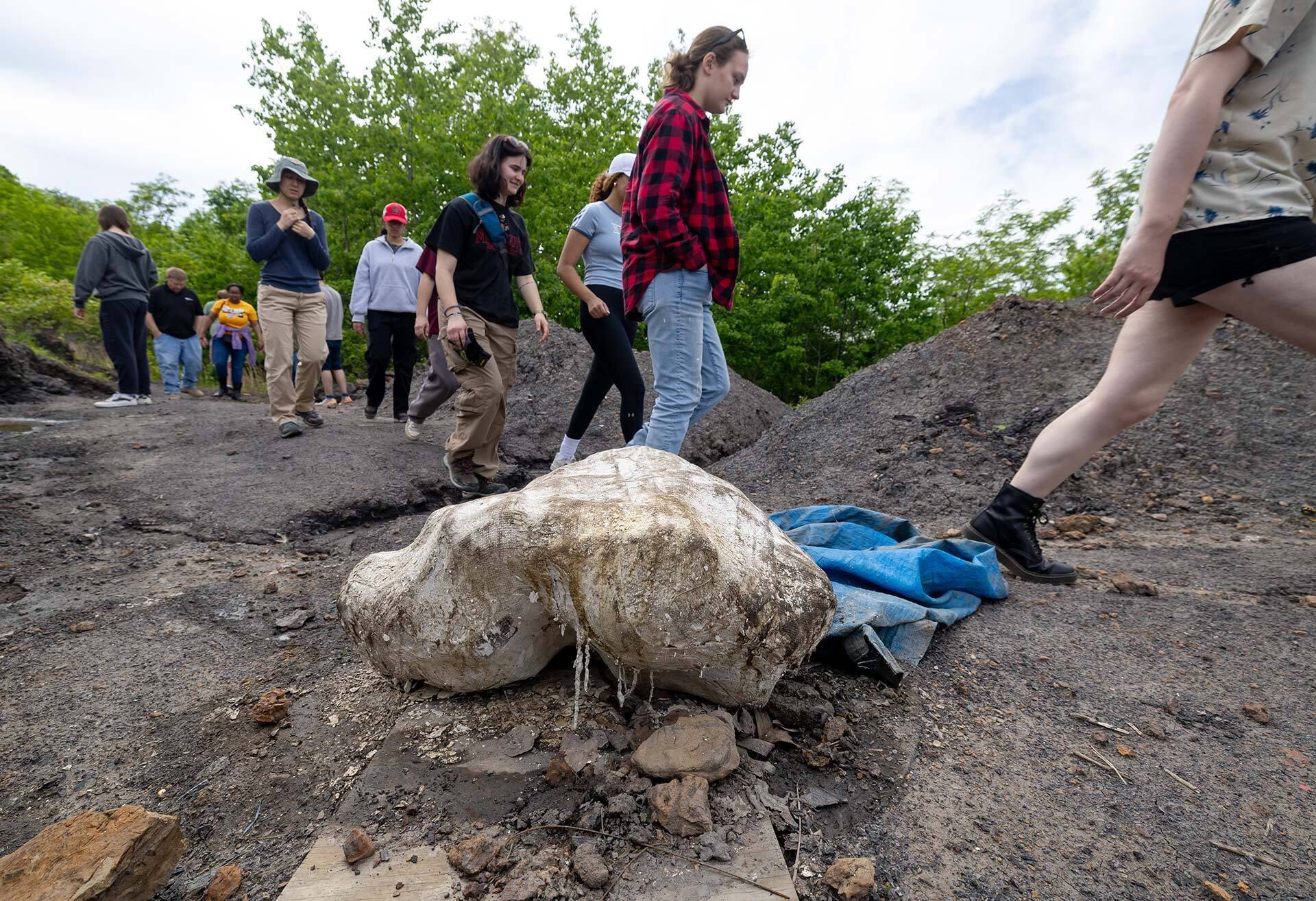 students walk past a plaster-covered fossil