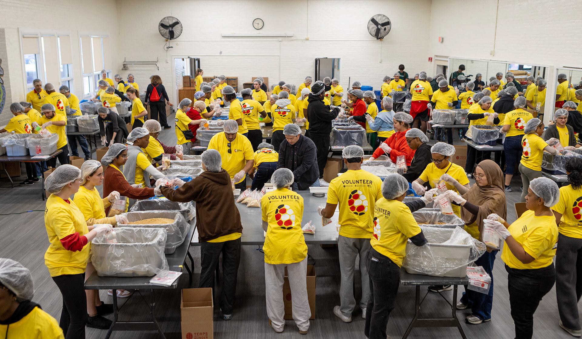 volunteers wearing yellow T-shirts and hairnets pack food