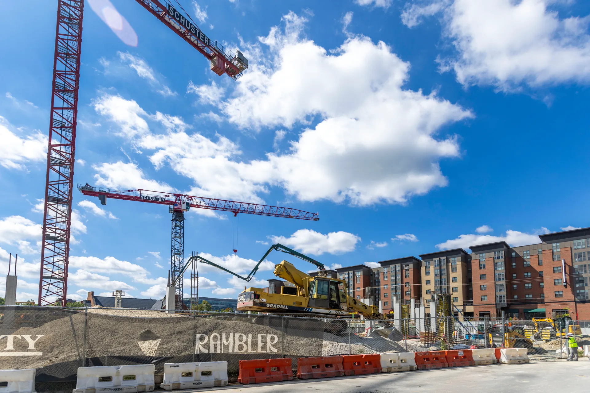 two cranes on construction site, with "Rambler" sign on fence