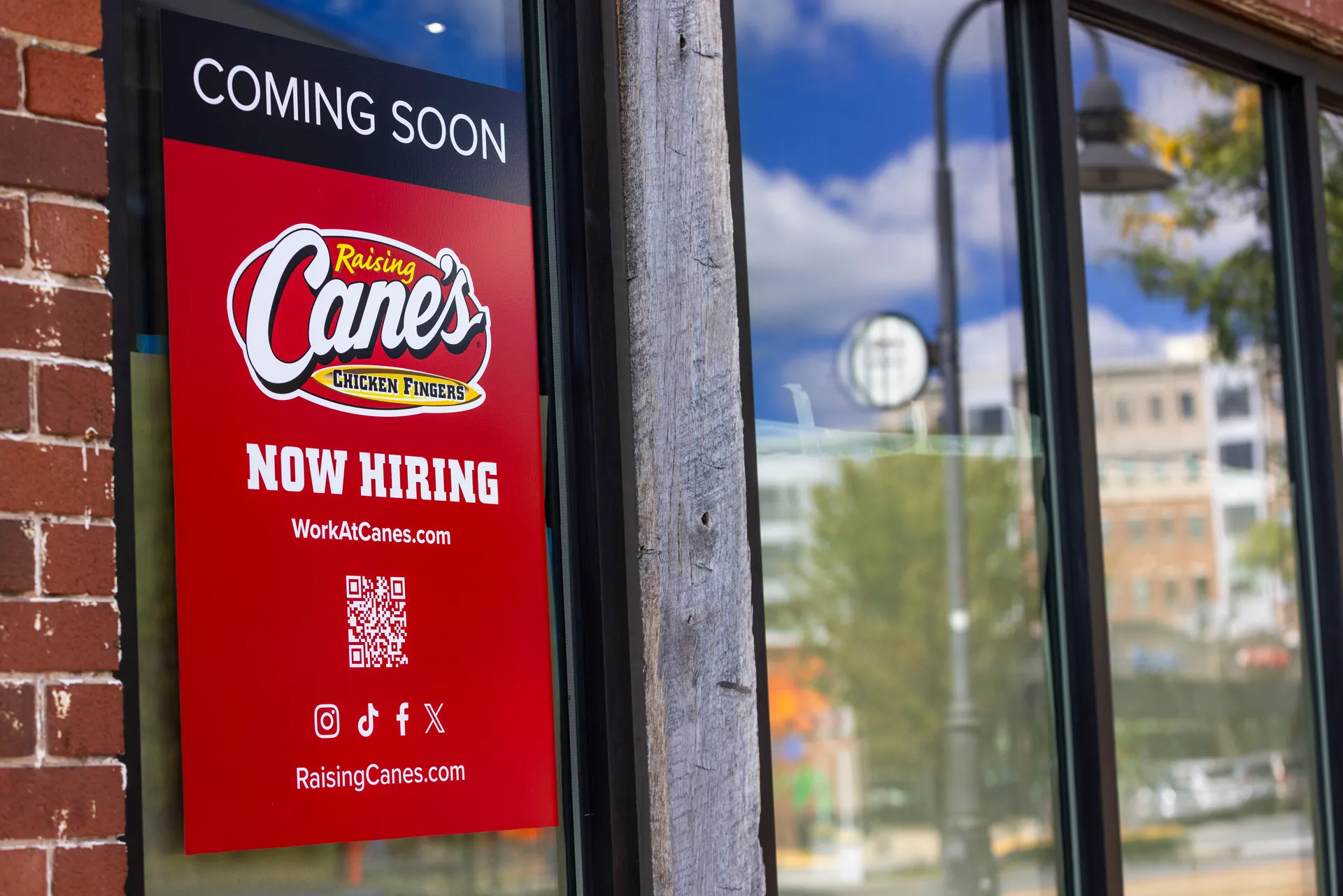 red sign that reads, "Coming soon: Raising Cane's Chicken Fingers. Now hiring"