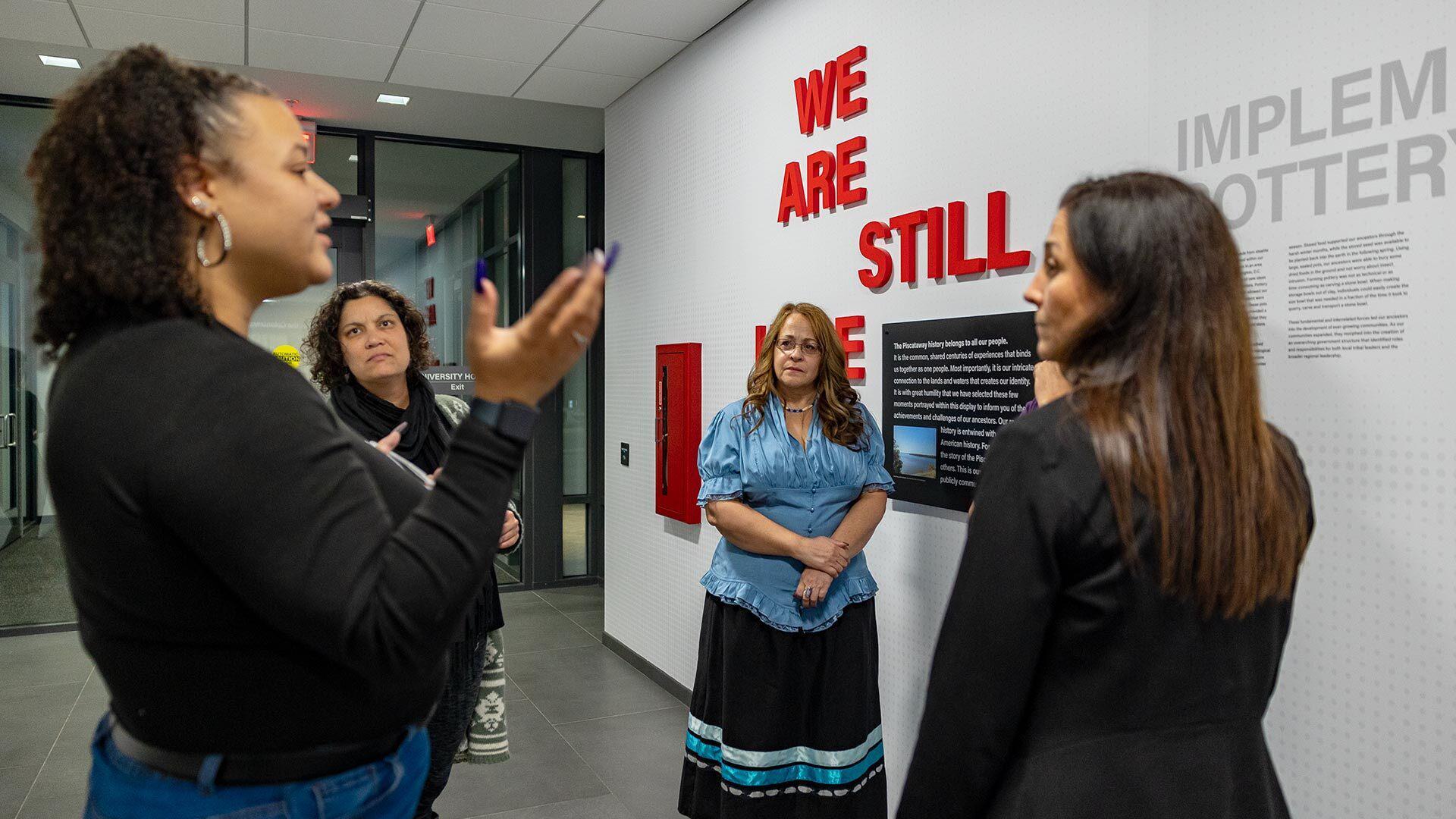 People talk in front of a wall that says "We Are Still Here"