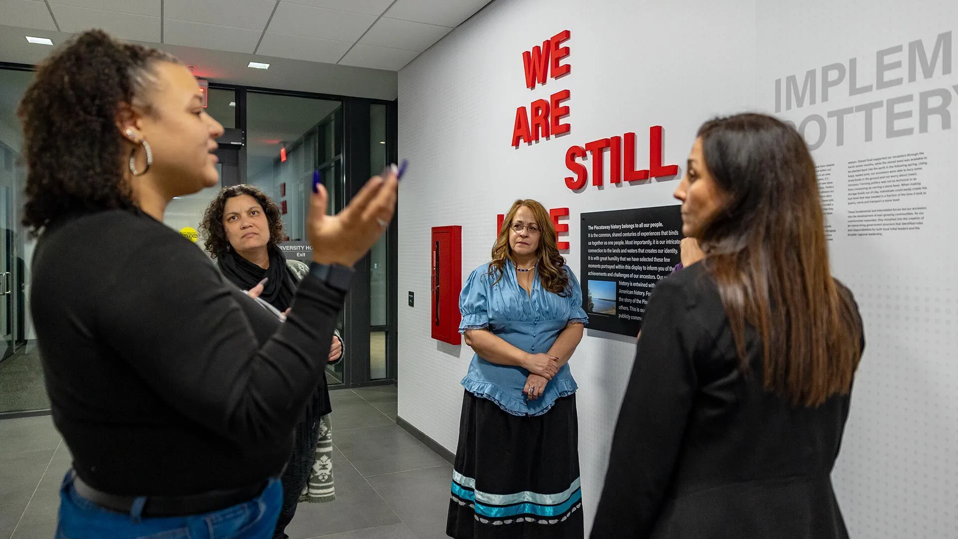 People talk in front of a wall that says "We Are Still Here"