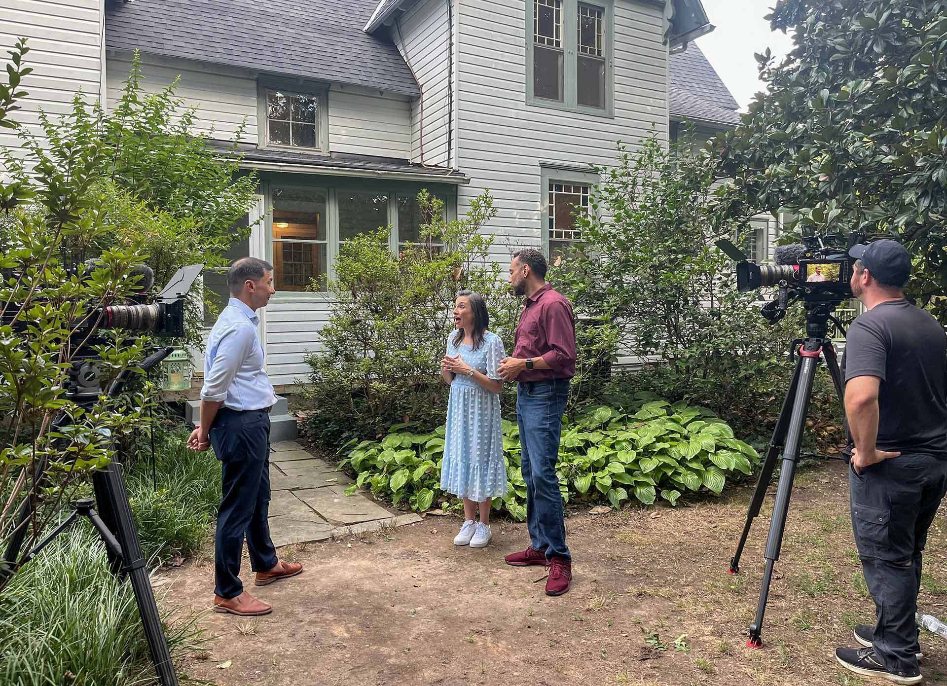 four people filming in front of house
