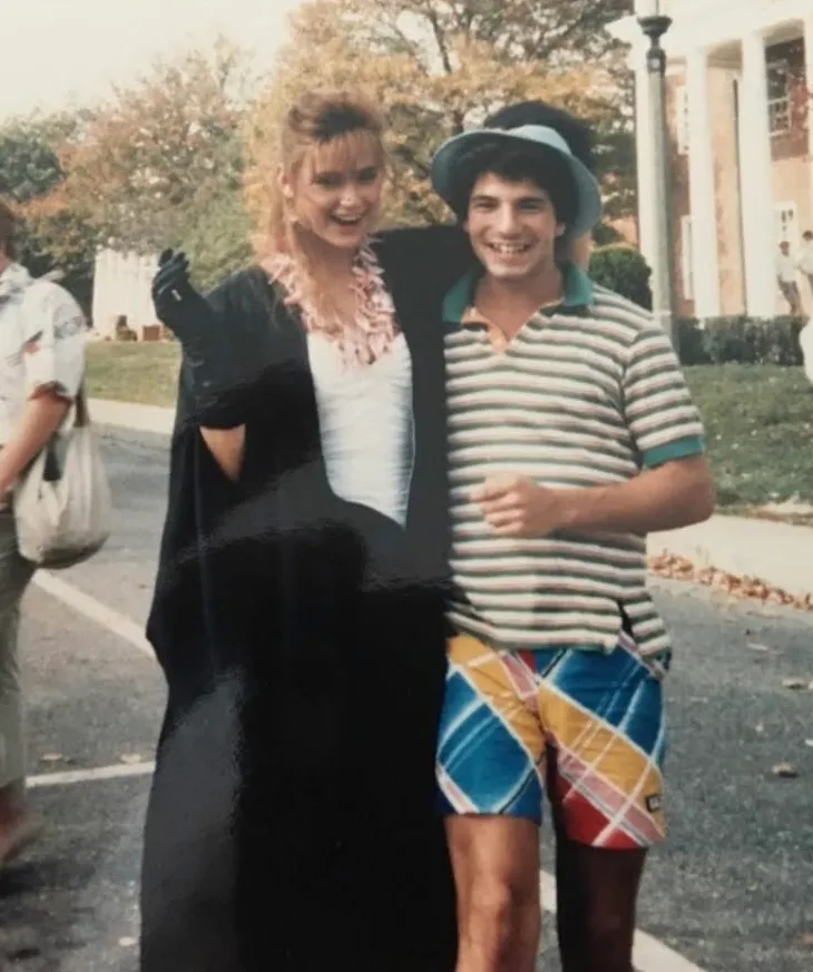Demi Moore in a white dress and black graduation gown holding a cigarette with Miguel Lopez in a visor, striped shirt and colorful shorts