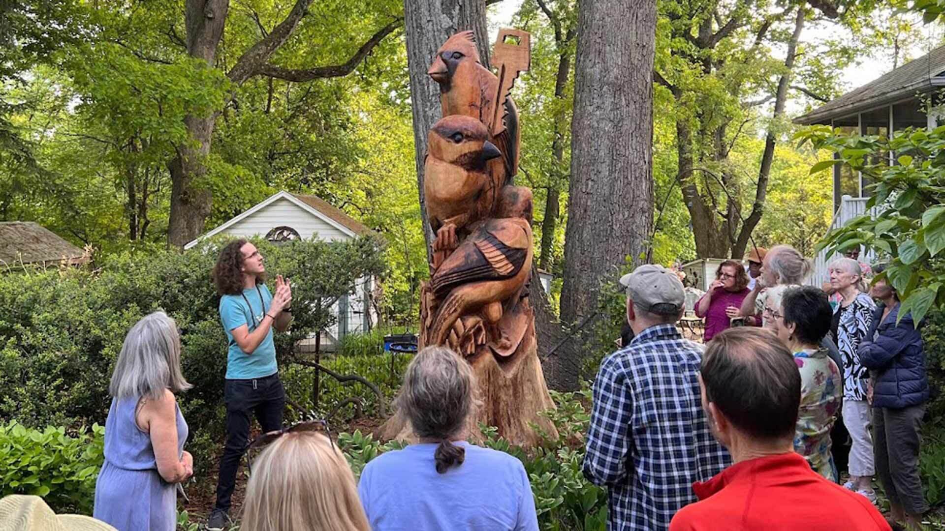 Colin Vale stands with a wood sculpture featuring birds and talks to a crowd