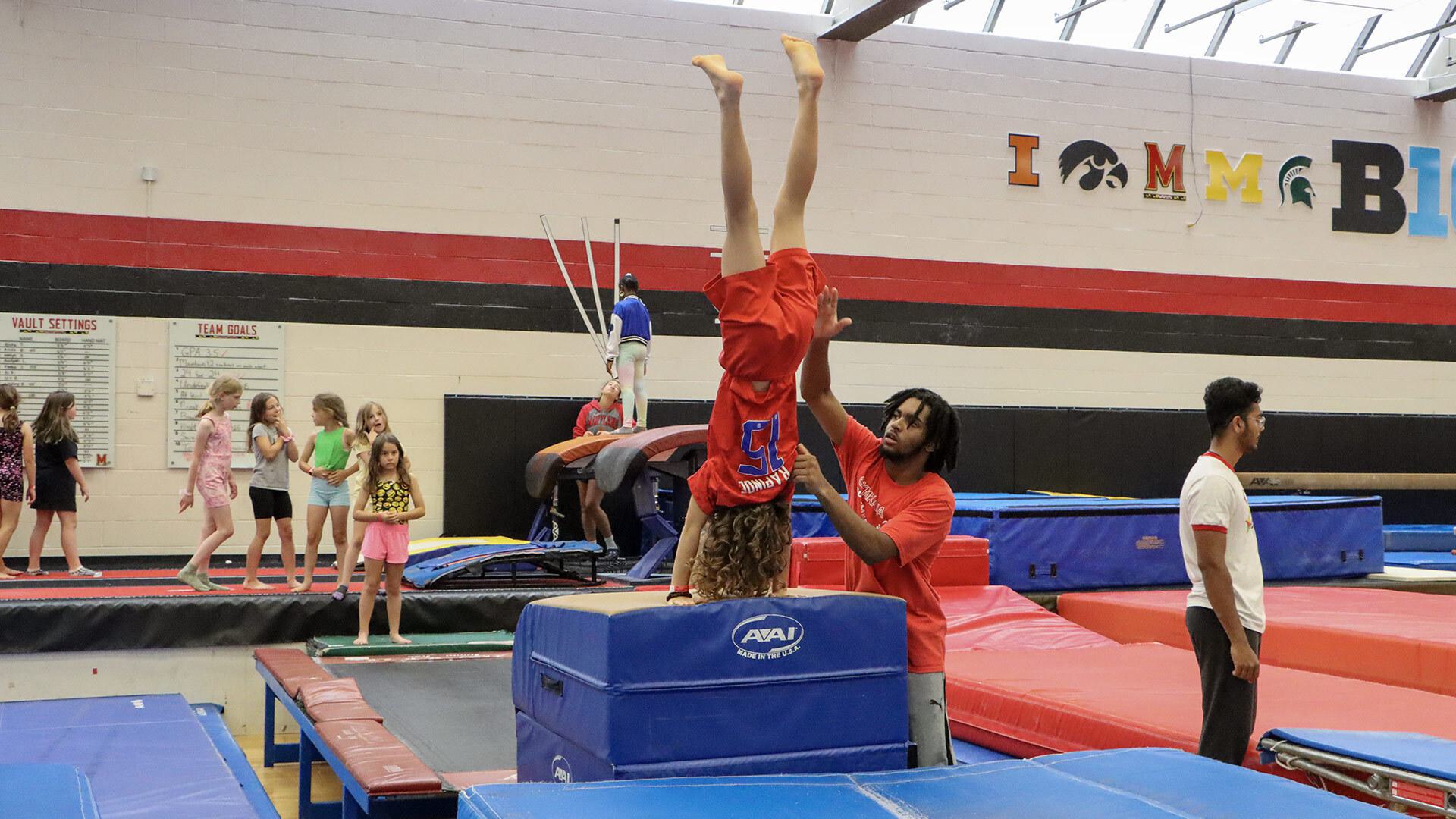 A counselor helps a girl in a handstand