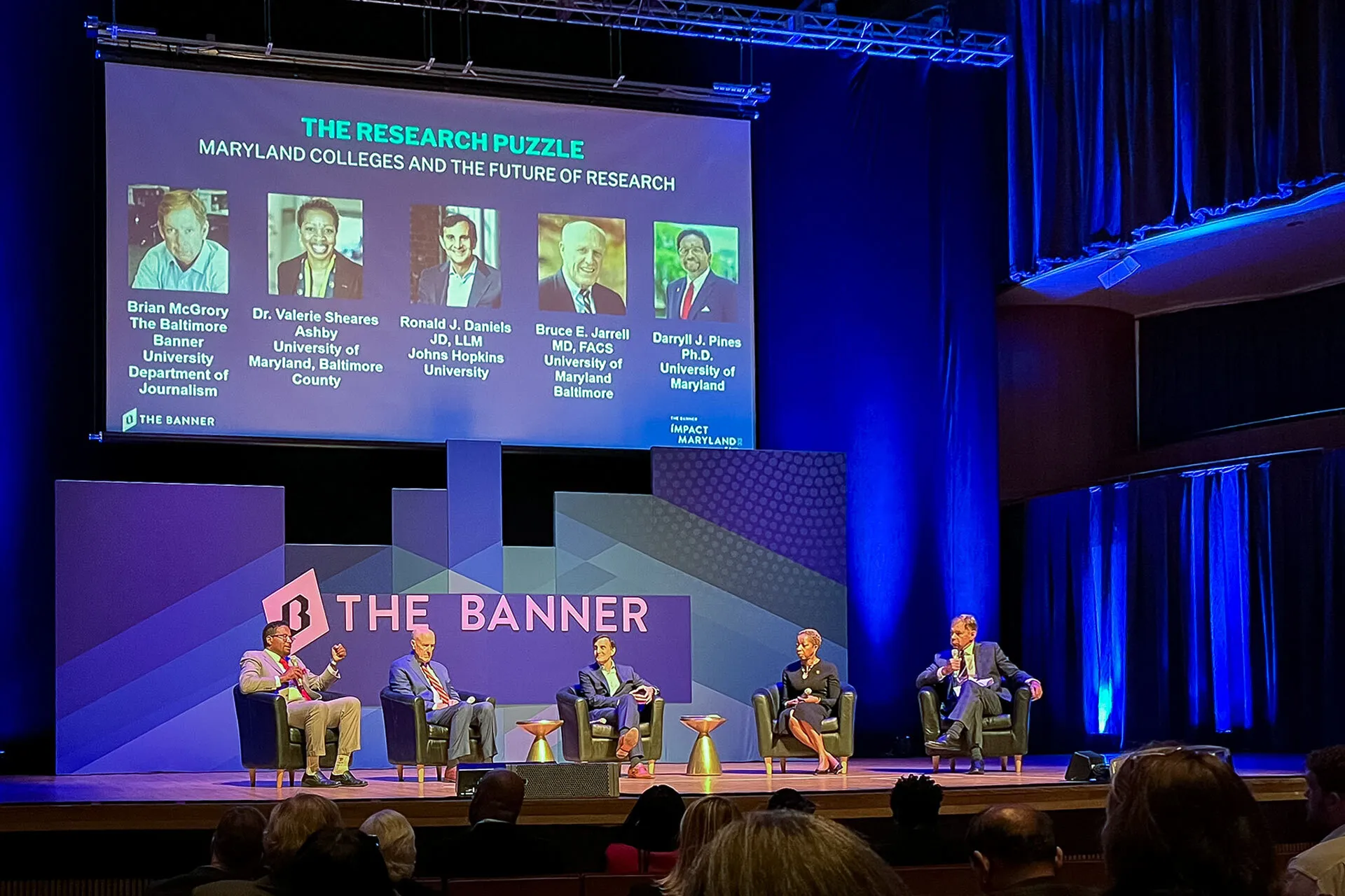 A group of people sit on a stage under a sign that says "The Banner."