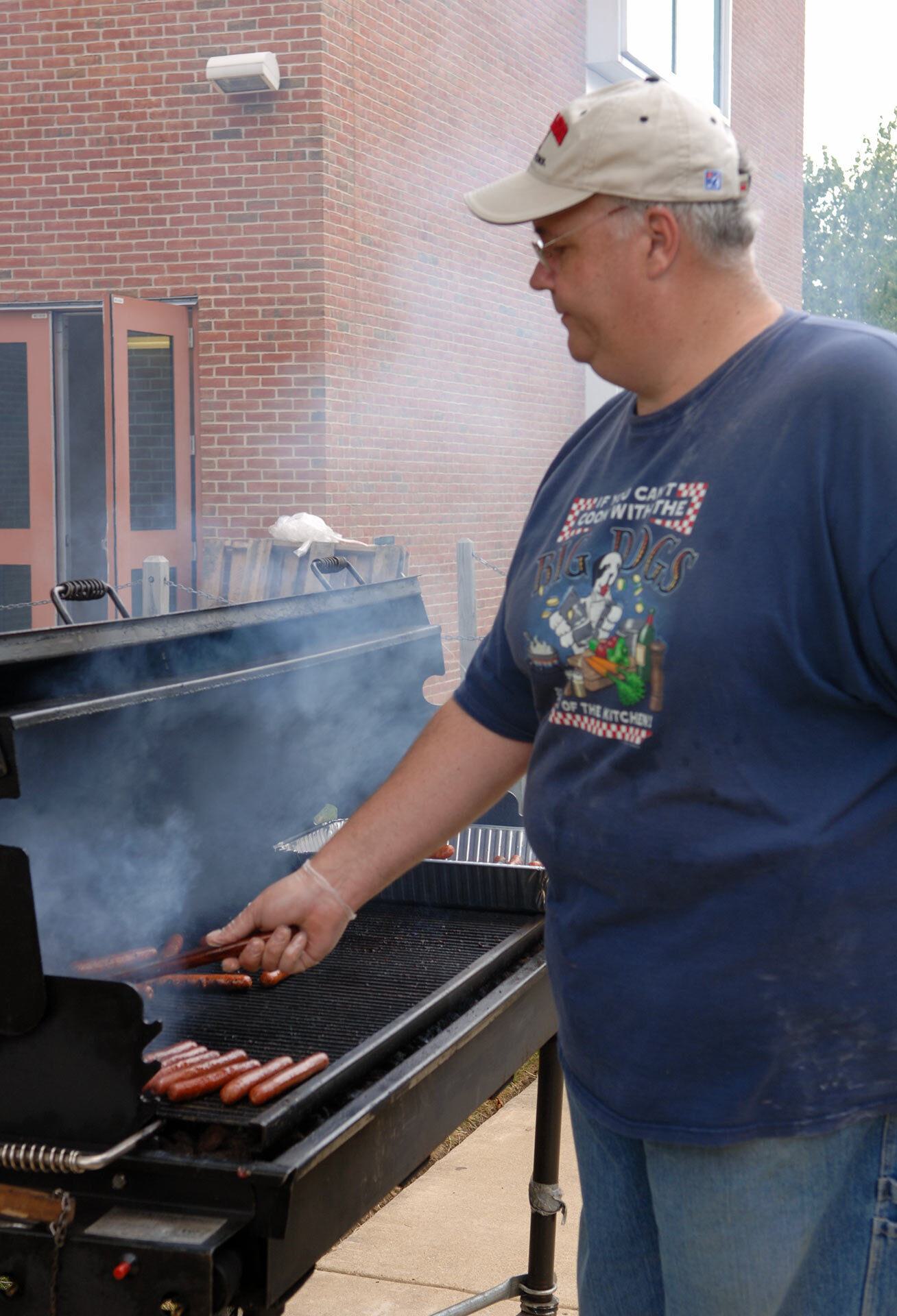 man cooks hot dogs on grill