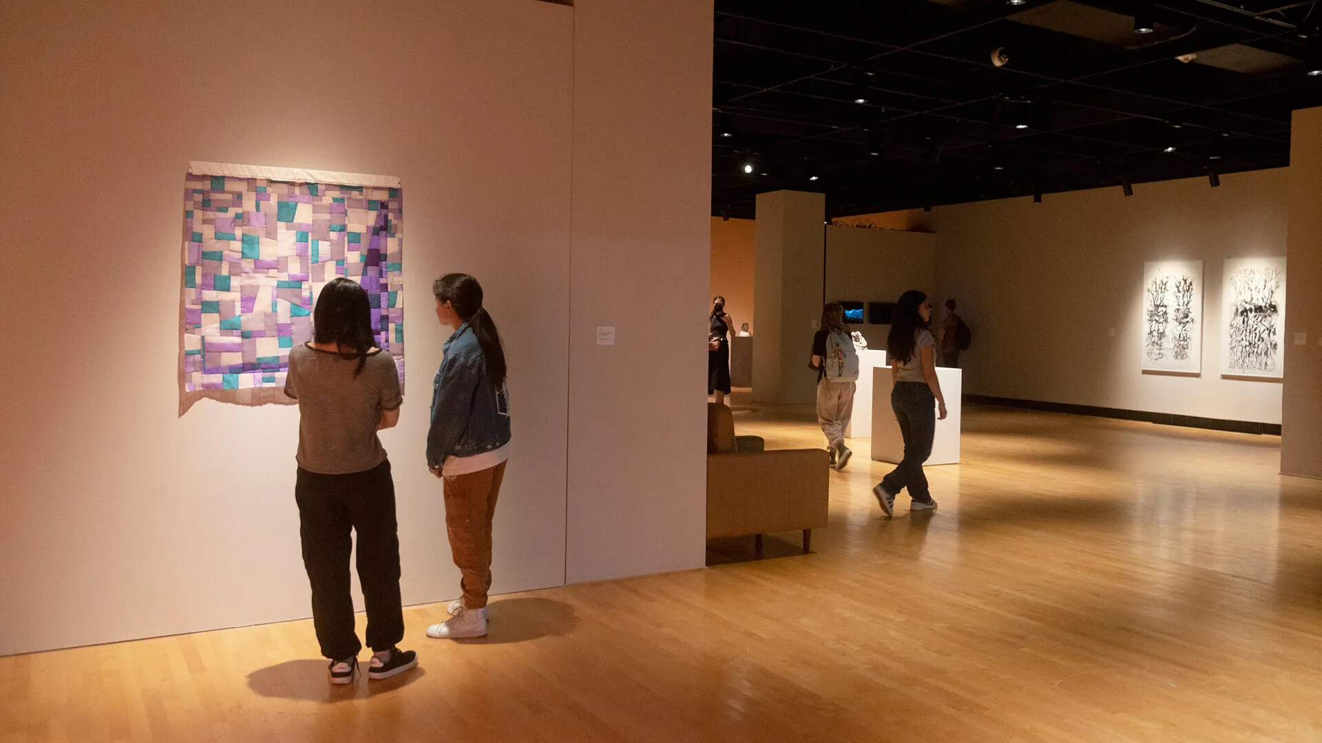 “bojagi”-style artwork hangs on wall, with two people viewing it