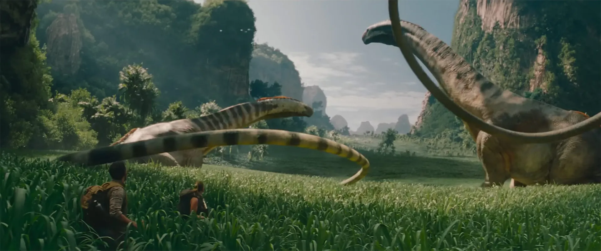 Two people watch plant-eating dinosaurs with long whiplash tails amidst tall grasses and cliffs